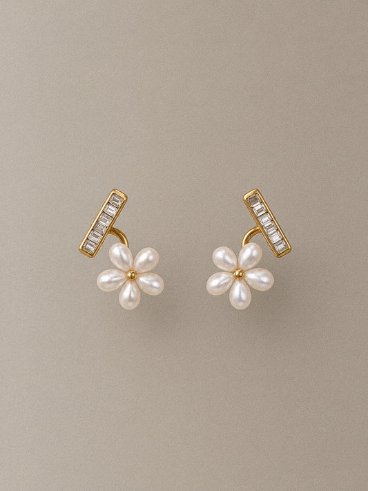 Pair of Fleurette gold-tone flower stud earrings with white faux pearl petals and clear rhinestone bars on a taupe background.