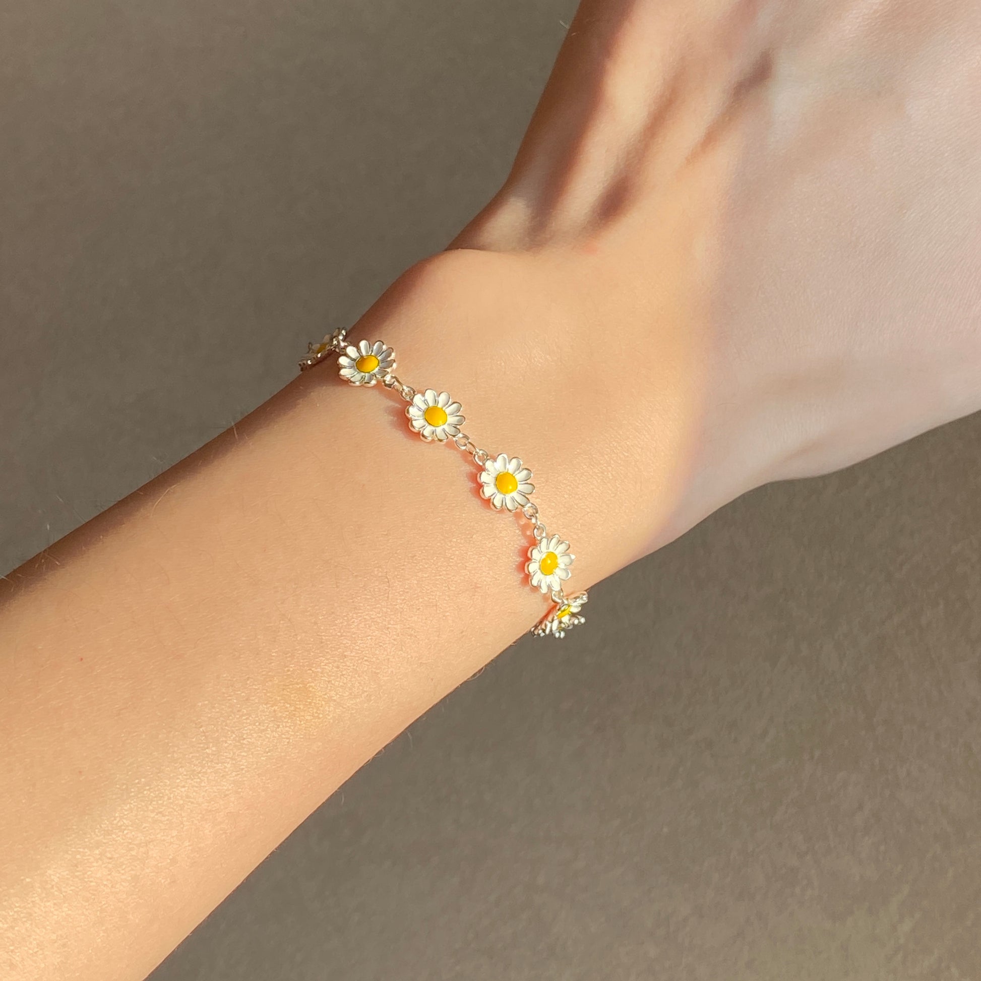 Dainty daisy charm bracelet on wrist in natural sunlight