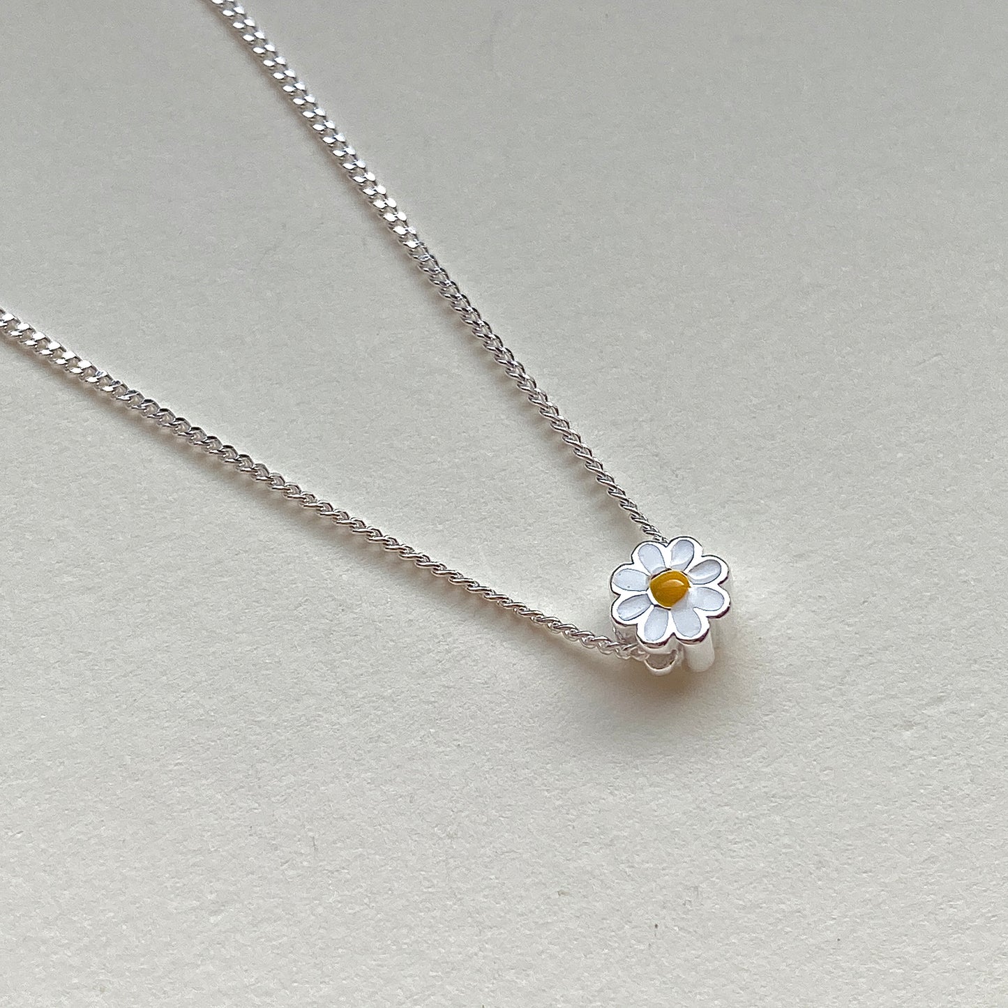 Macro of white-and-yellow enamel daisy bead threaded on chain
