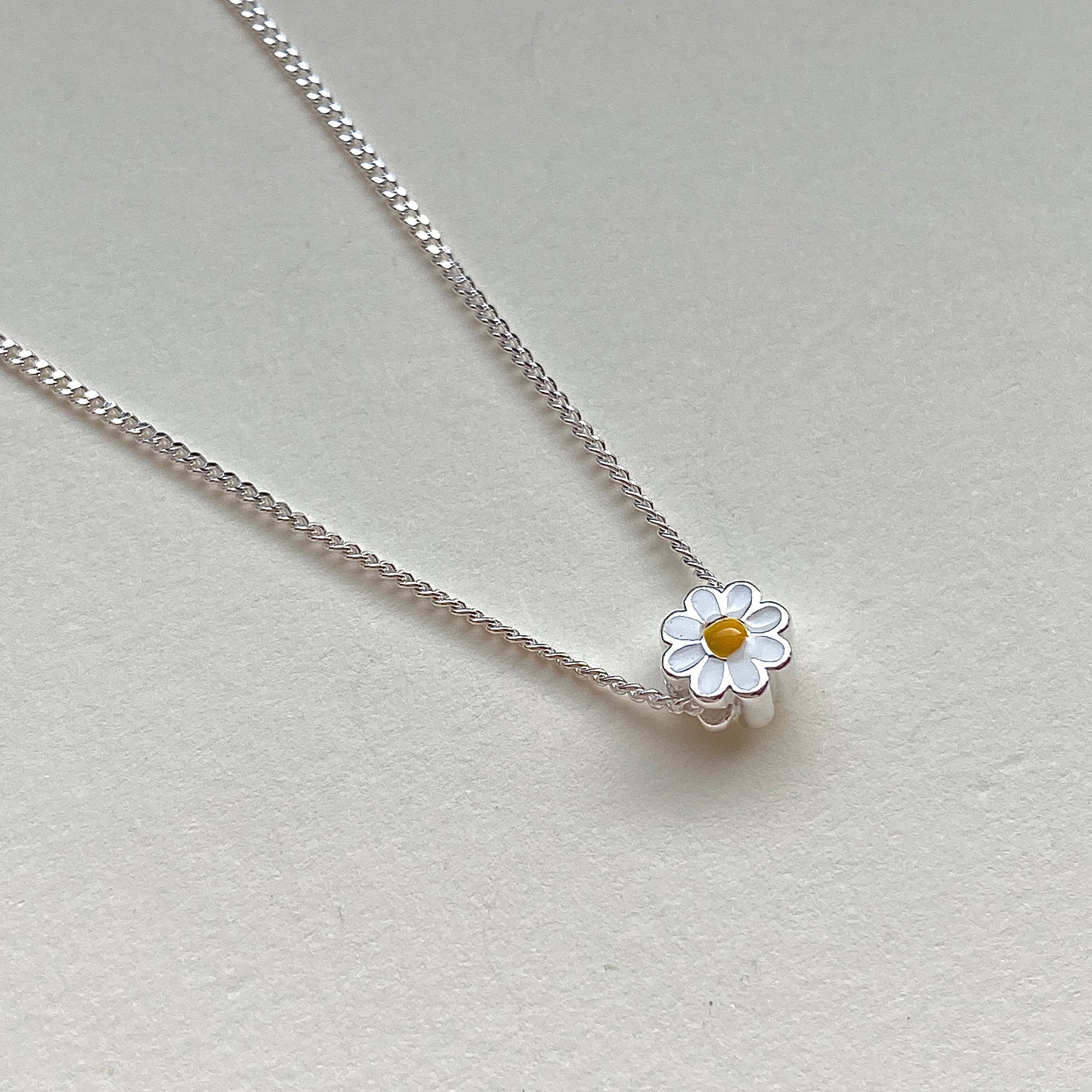 Macro of white-and-yellow enamel daisy bead threaded on chain