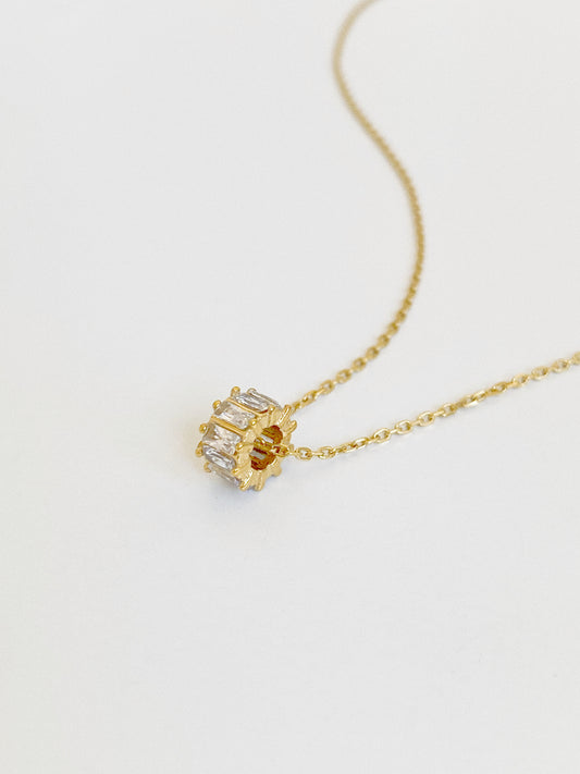 Macro close-up of the gold barrel charm set all around with clear baguette-cut cubic zirconia, showing its three-dimensional spinning-wheel form