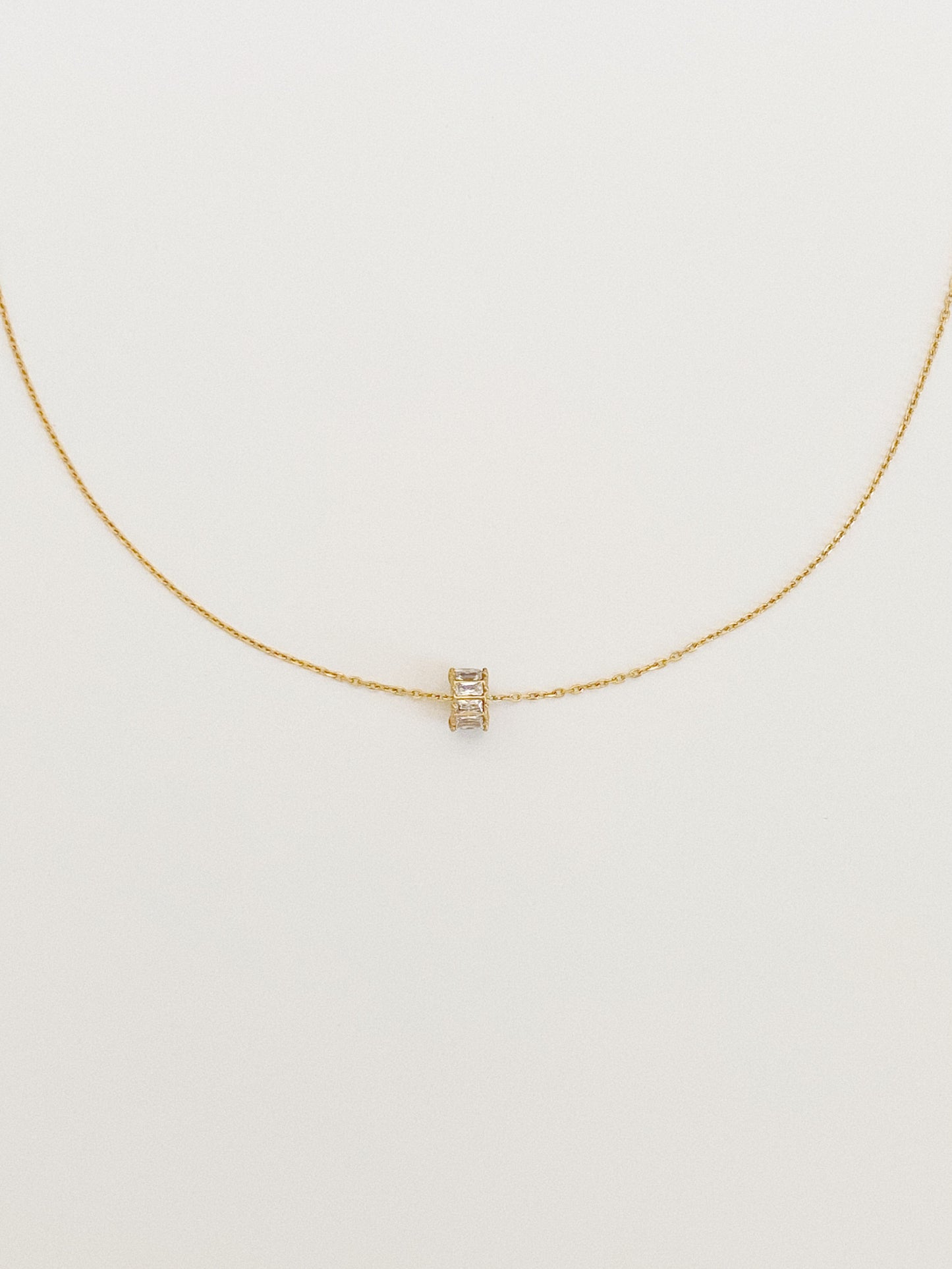 Full length flat lay of a dainty gold cable chain necklace with a small spinning zircon lucky charm centred at the front