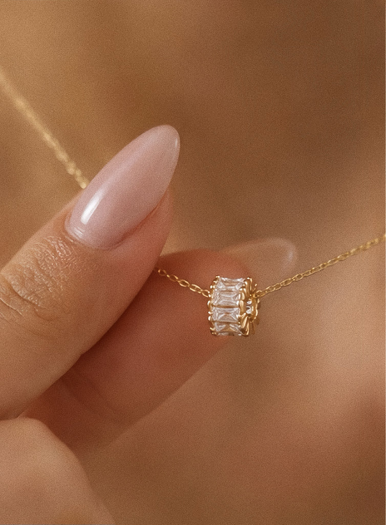 Fingertips holding the tiny gold zircon lucky wheel charm in warm light, showing its petite scale and sparkle against skin