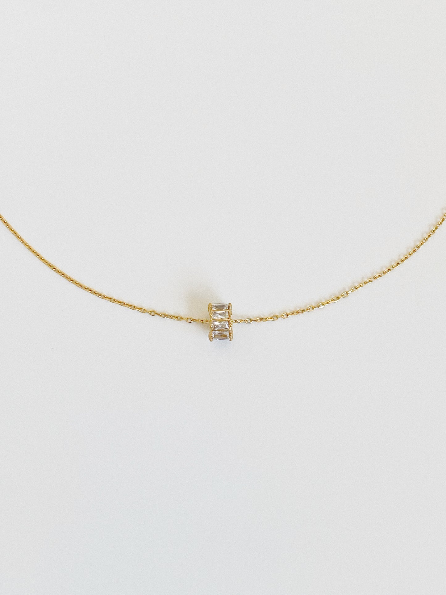 Gold waterproof lucky charm necklace with a tiny baguette zircon spinning wheel pendant, shown flat from the front on a soft grey background