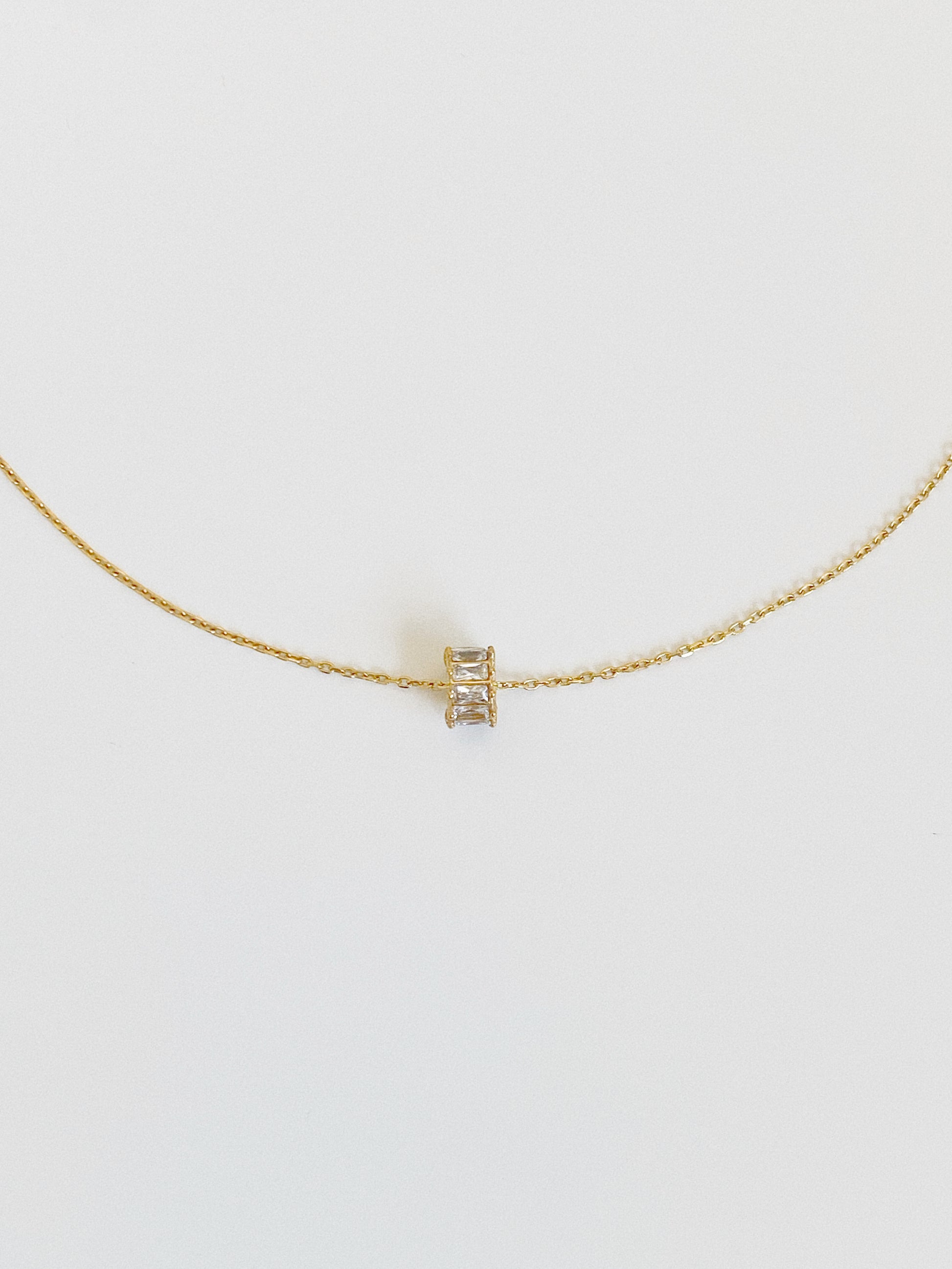 Gold waterproof lucky charm necklace with a tiny baguette zircon spinning wheel pendant, shown flat from the front on a soft grey background