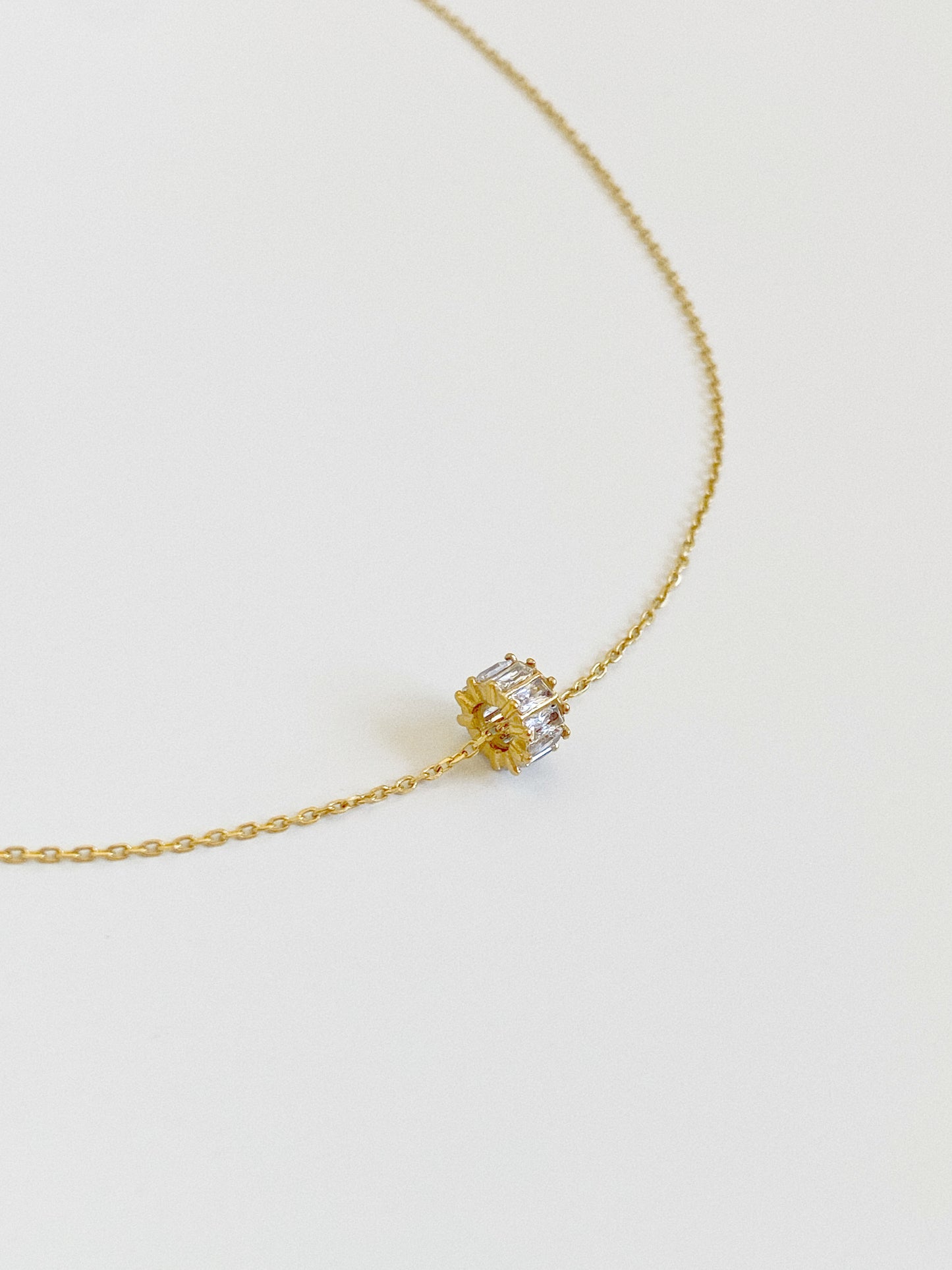Close angled view of the Fortuna gold zircon wheel charm showing the barrel shape and prong-set baguette stones on a fine cable chain