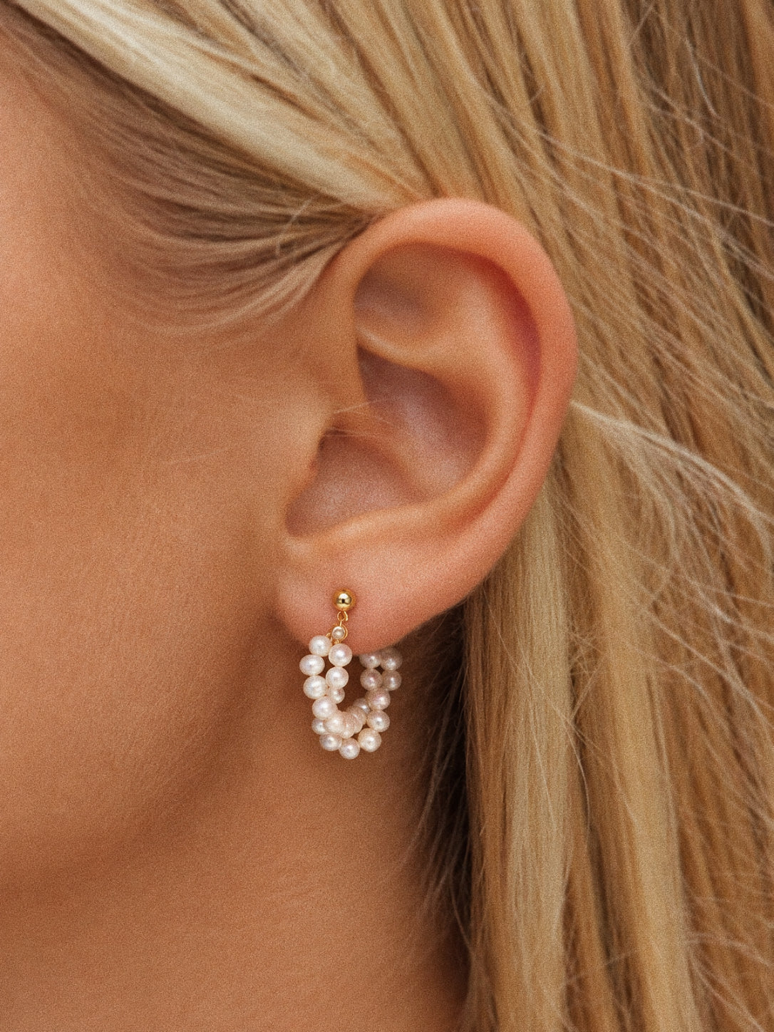 Garland freshwater pearl hoop earring worn on an ear, with twisted white pearl strands beneath a small gold-tone stud.