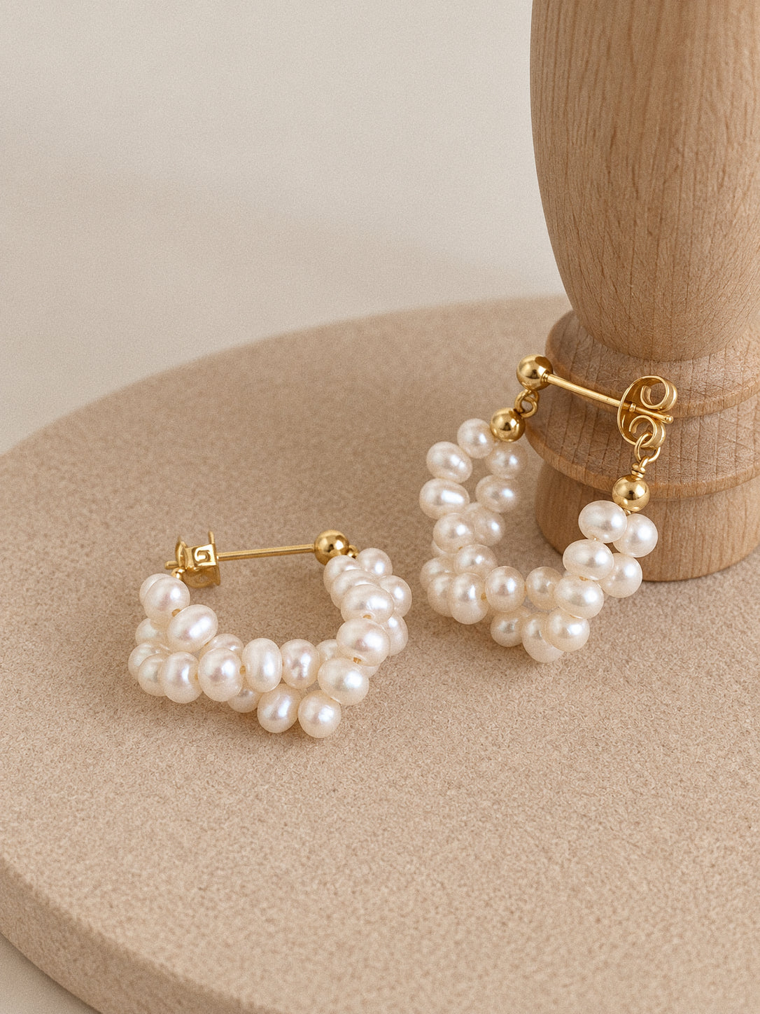 Close-up of Garland hoops beside a wooden stand, showing the irregular freshwater pearls and gold-plated fittings.