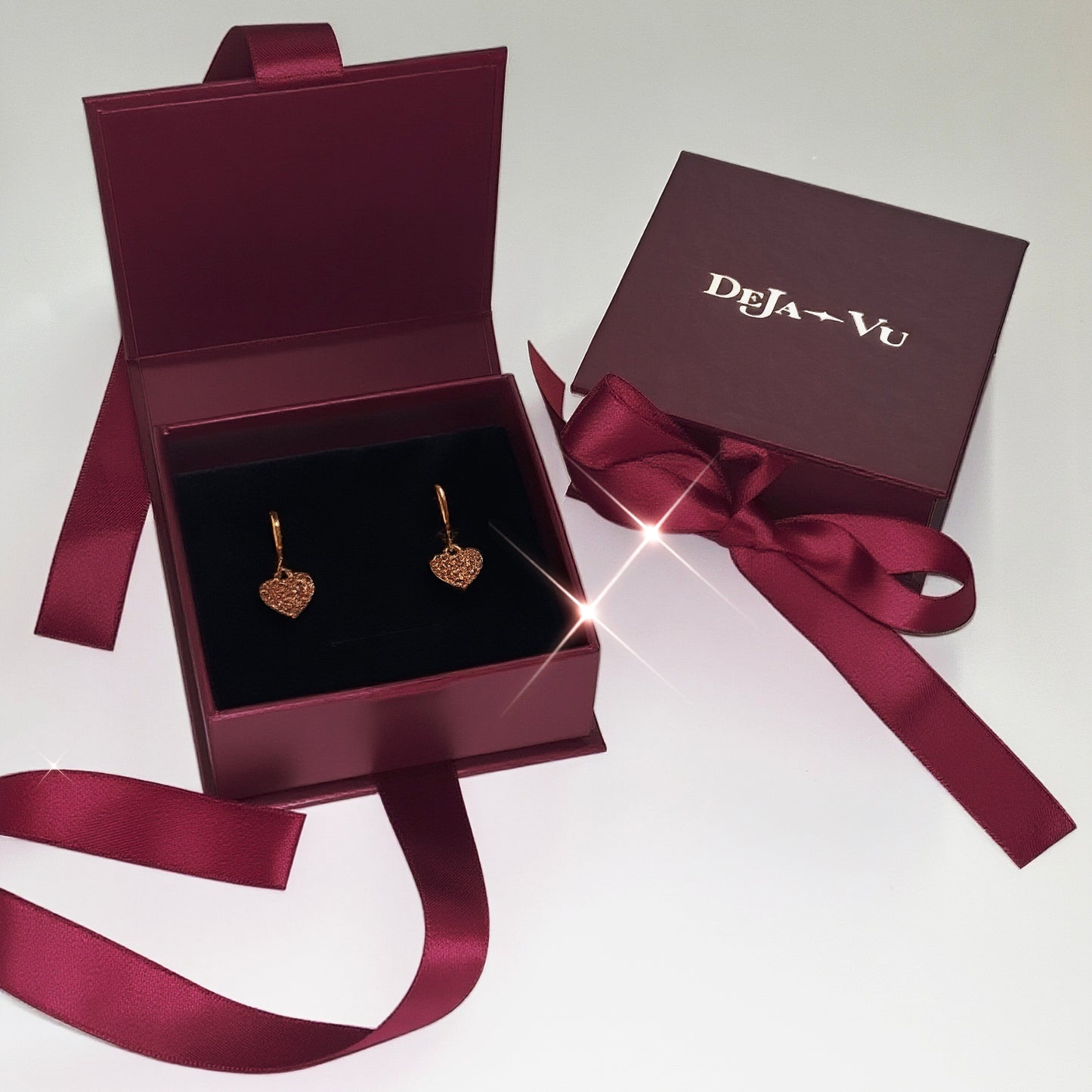 Deja vu burgundy luxury jewellery box containing pink heart earrings, illuminated for a premium gifting look.