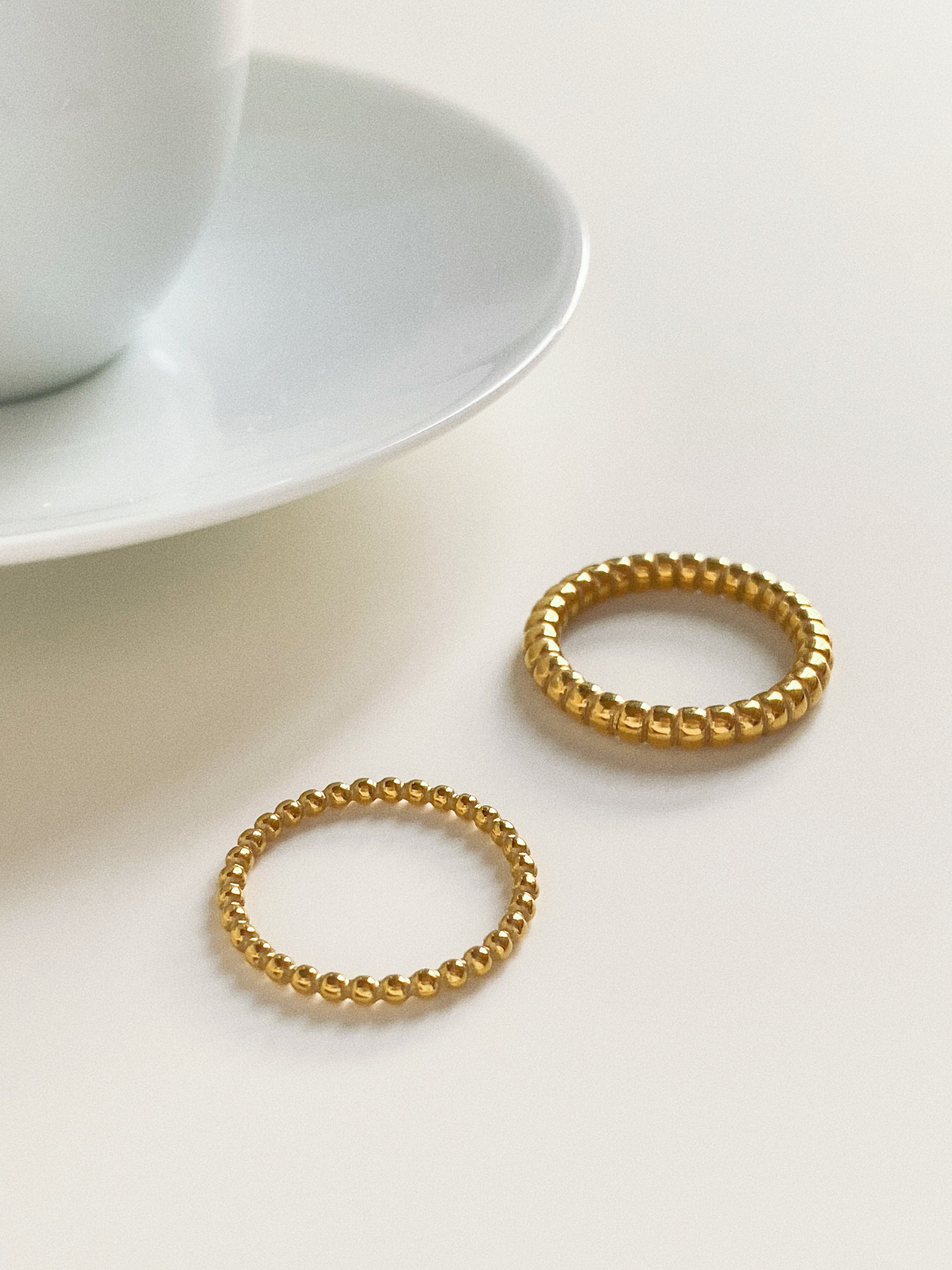 Two gold beaded rings placed next to a coffee cup for a modern lifestyle aesthetic.