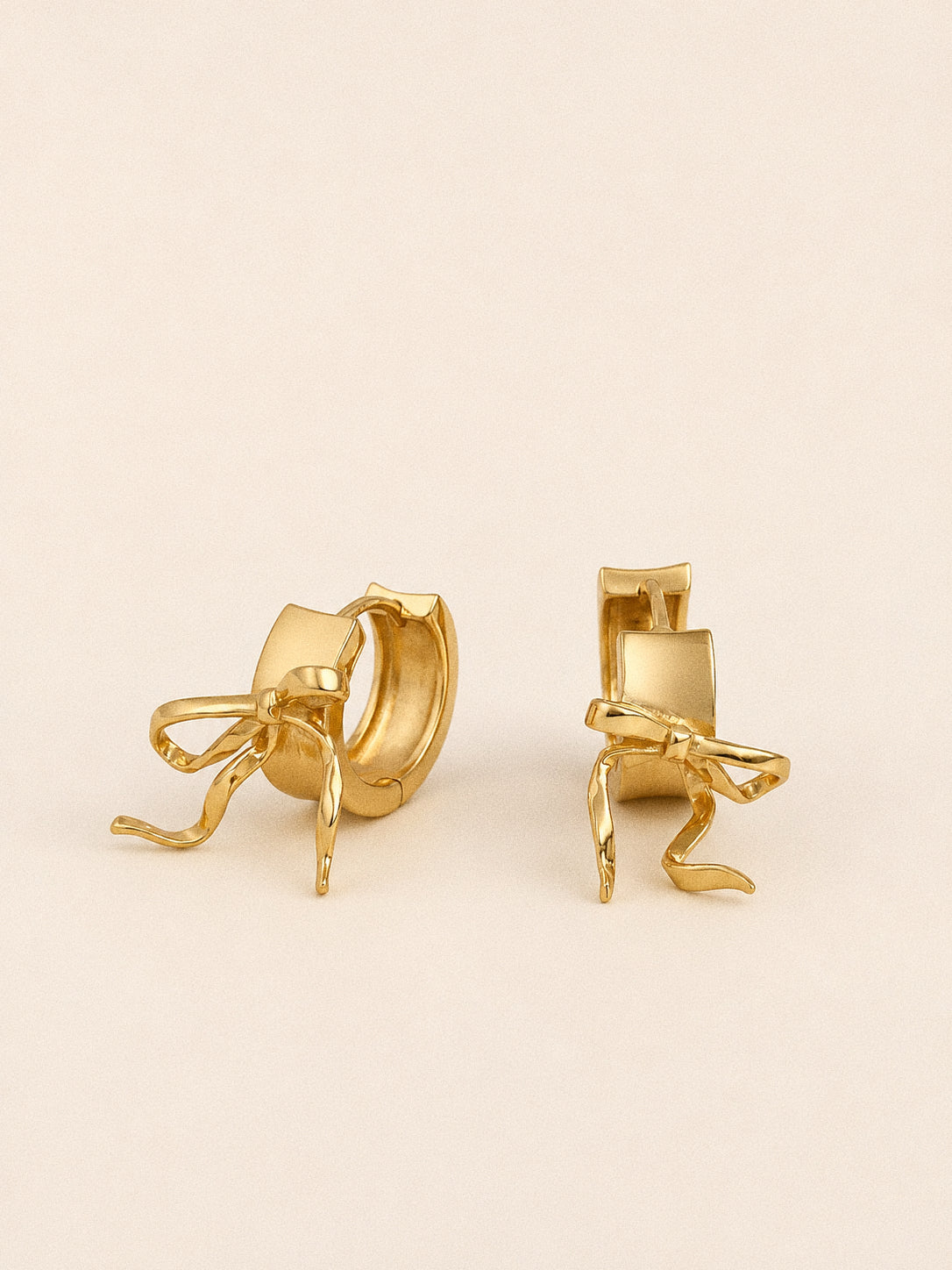 Gold bow huggie hoop earrings at an angle, showing the wide band and sculpted ribbon bow in profile.