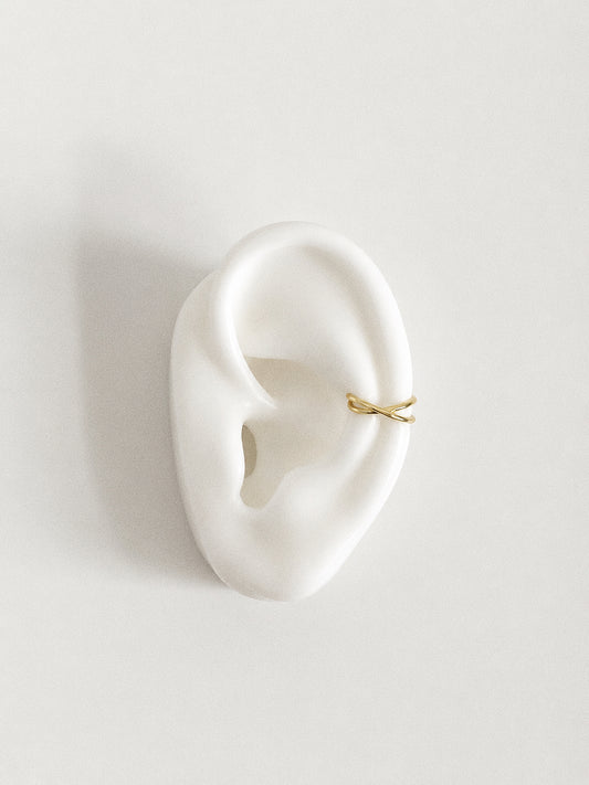 Gold criss cross ear cuff shown positioned on the cartilage of a ceramic ear display, slide-on cuff for unpierced ears