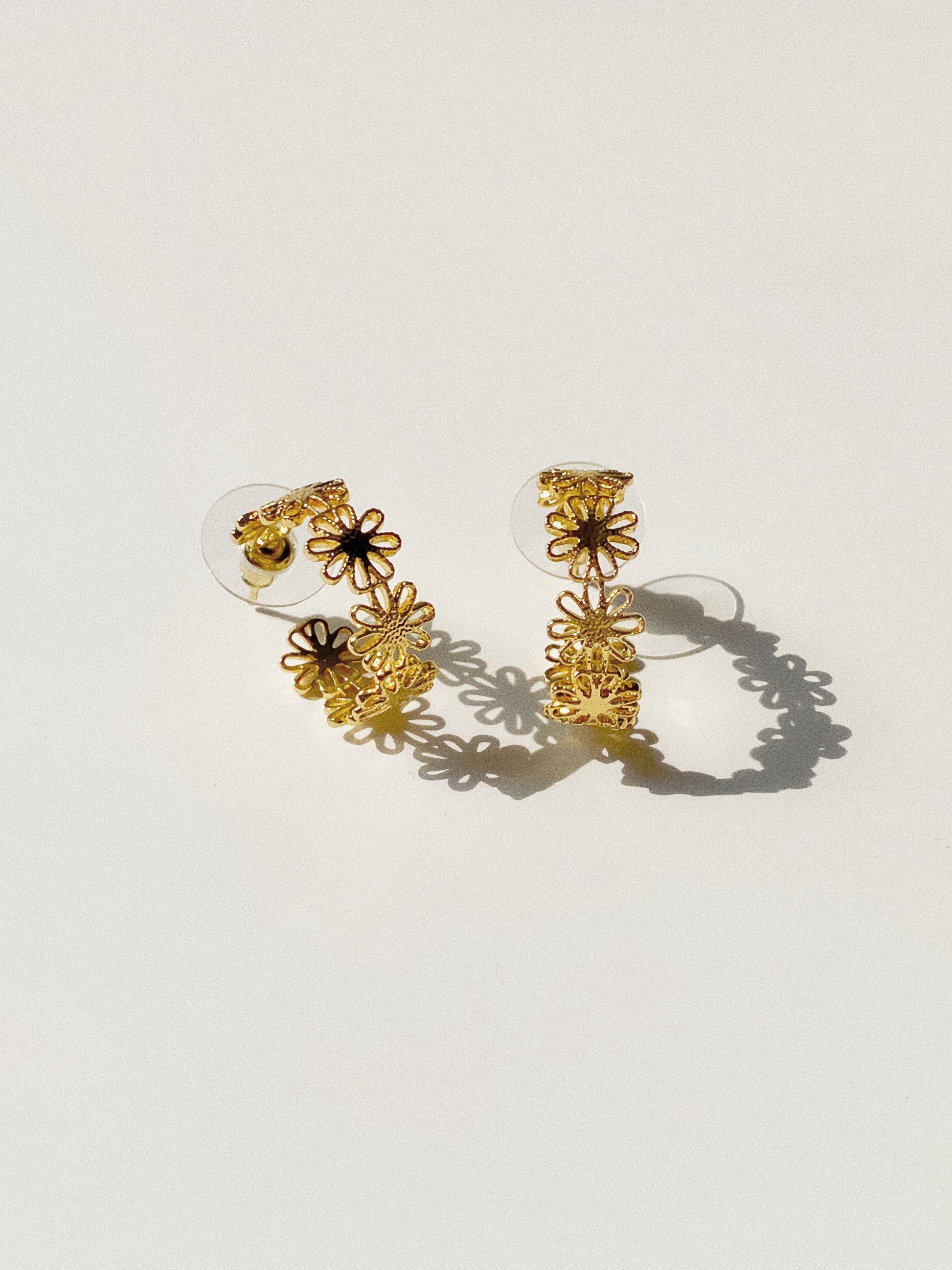 Gold daisy lace open hoop earrings showing intricate cut-out floral detail and flower shadow