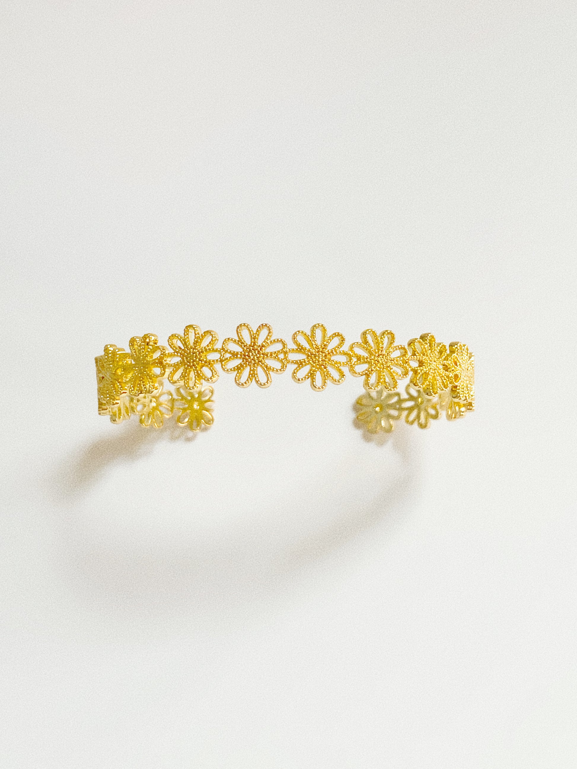 Gold daisy lace open cuff bracelet showing intricate cut-out daisy chain detail