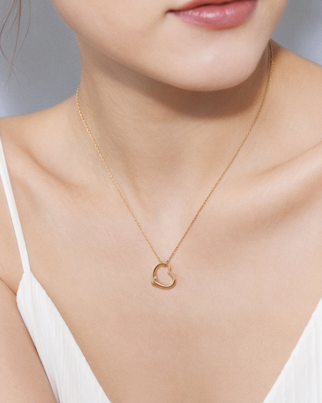 Model wearing a dainty gold floating open heart necklace sitting just below the collarbone with a white top