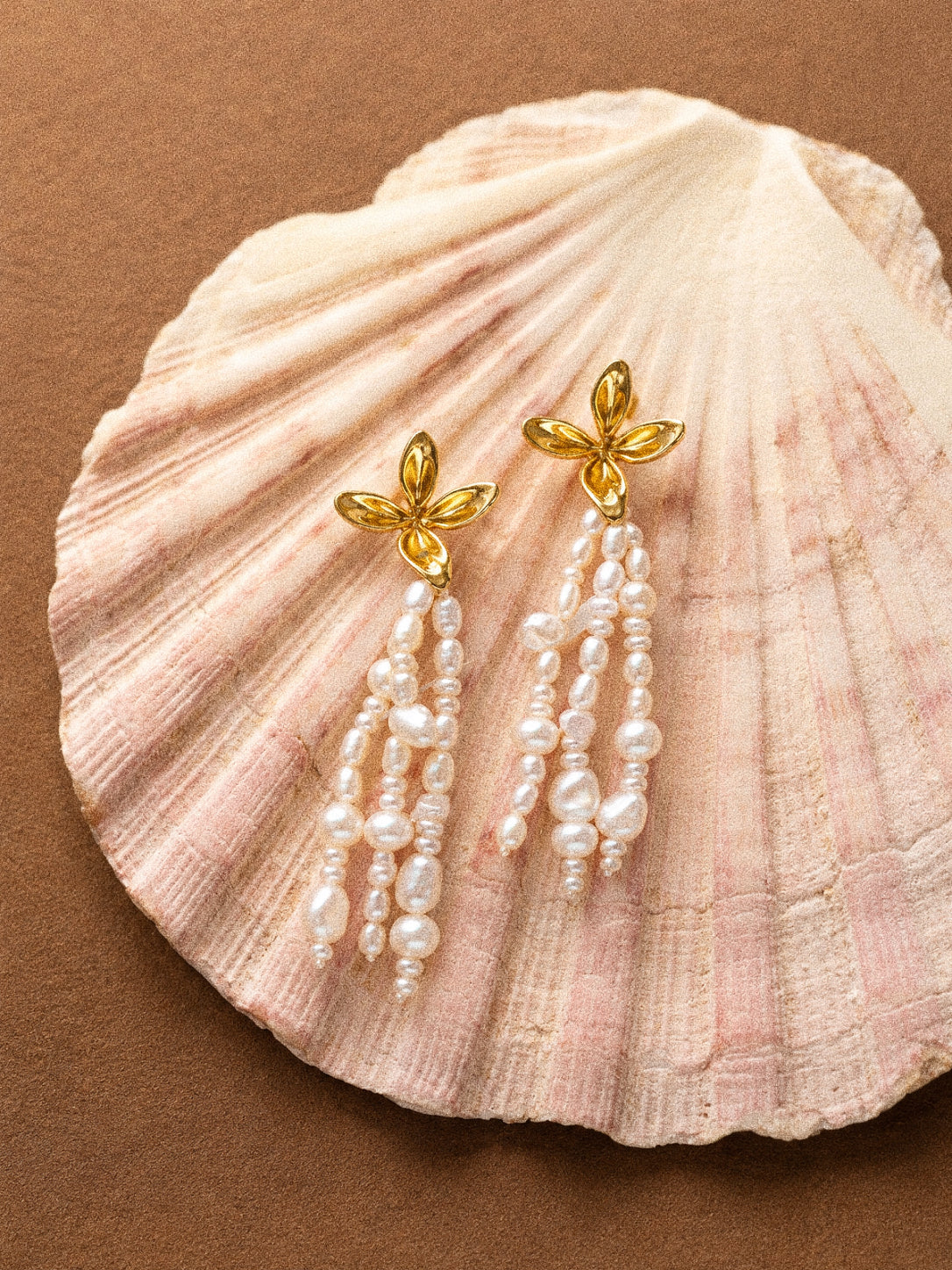 Gold flower and freshwater baroque pearl tassel earrings displayed on a large pale seashell.