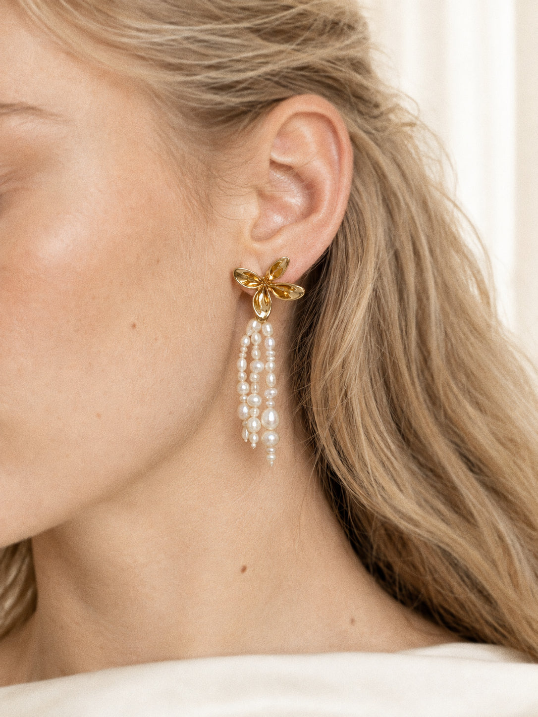 Close view of a Fleur gold flower pearl tassel earring worn on the ear, showing its sculptural petals and baroque pearls.