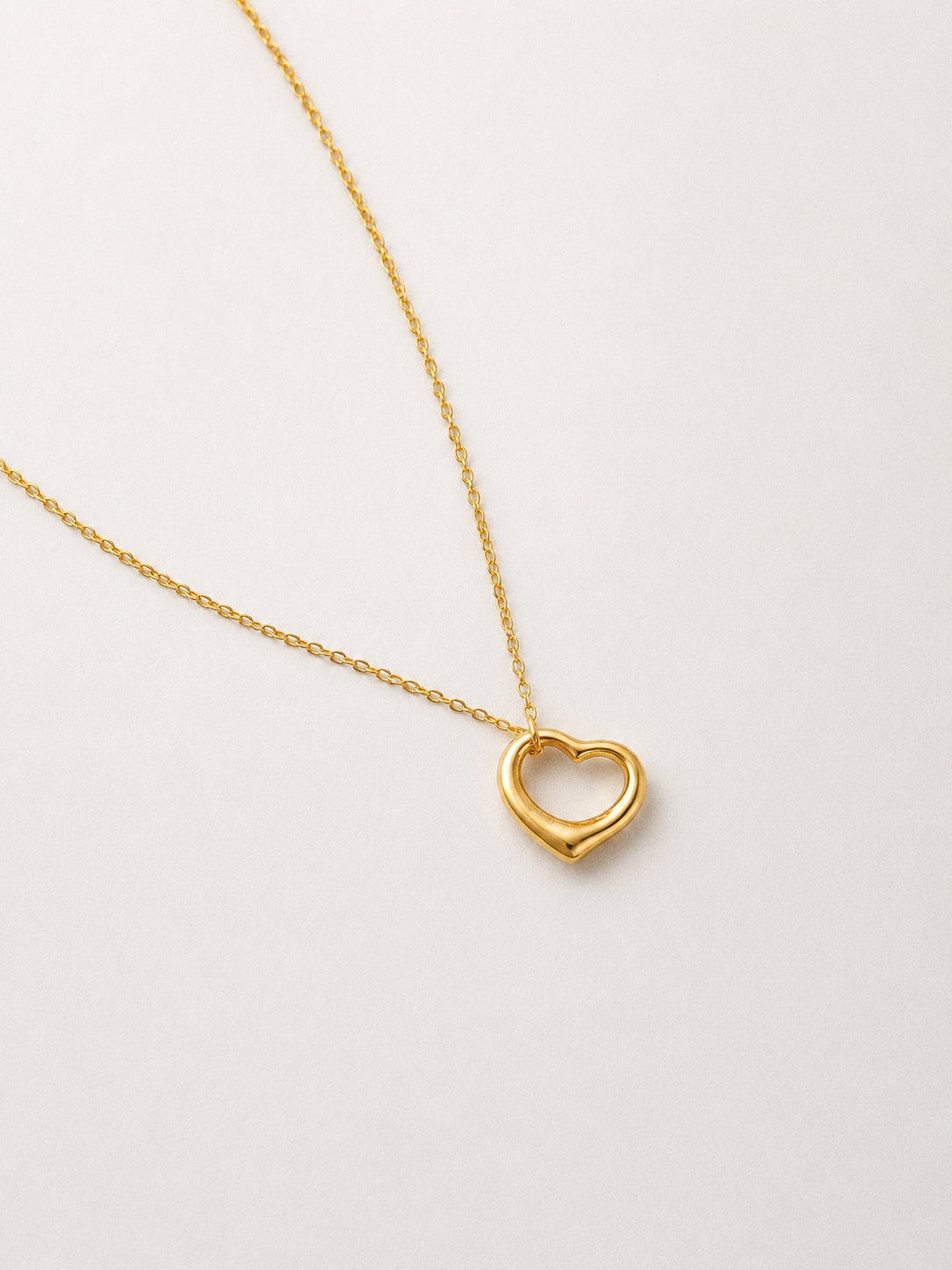 Angled view of a gold open heart pendant necklace showing the smooth sculptural floating heart on a delicate chain
