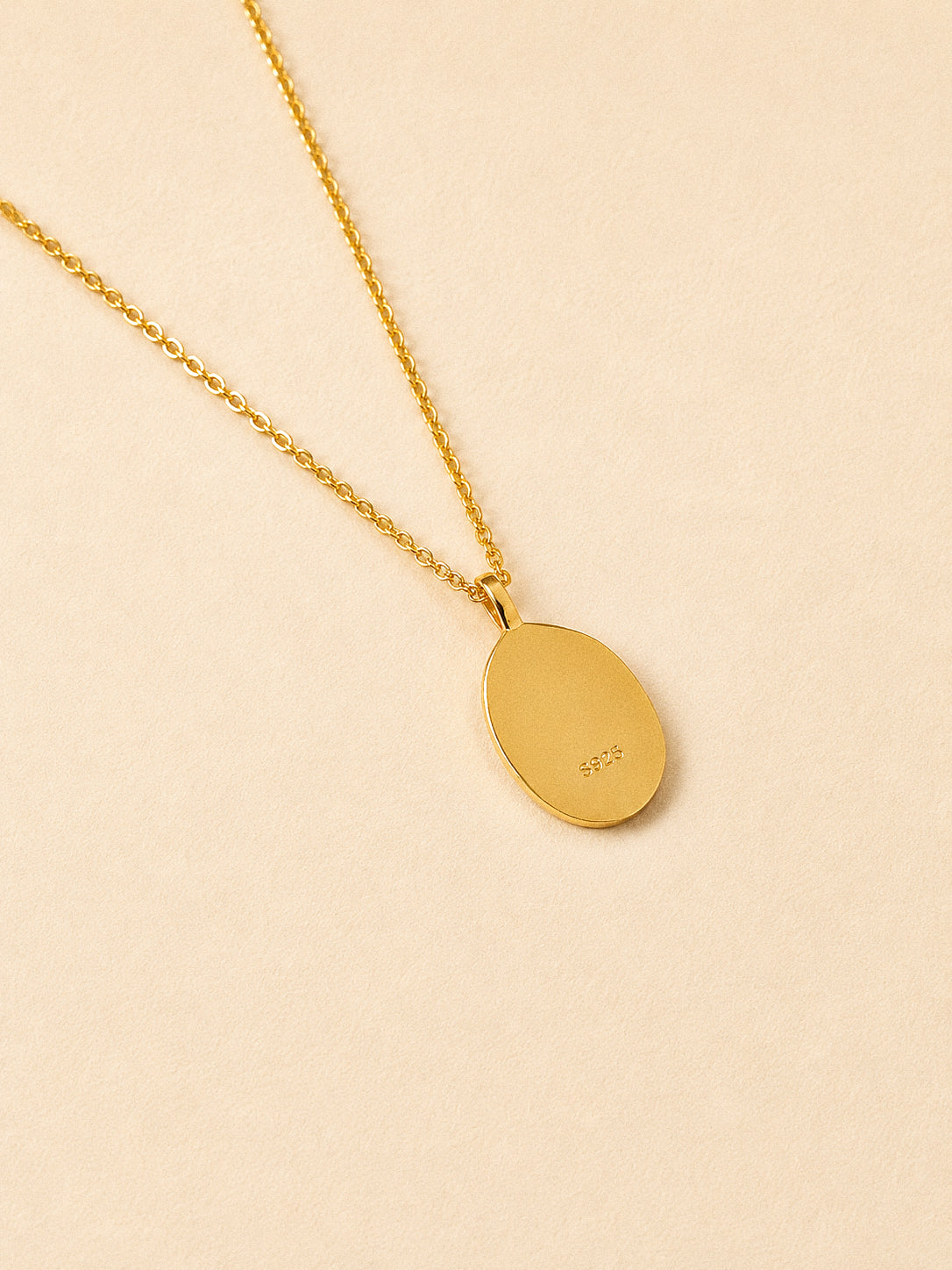Reverse of the gold oval rose pendant stamped S925 on a fine gold chain, cream background