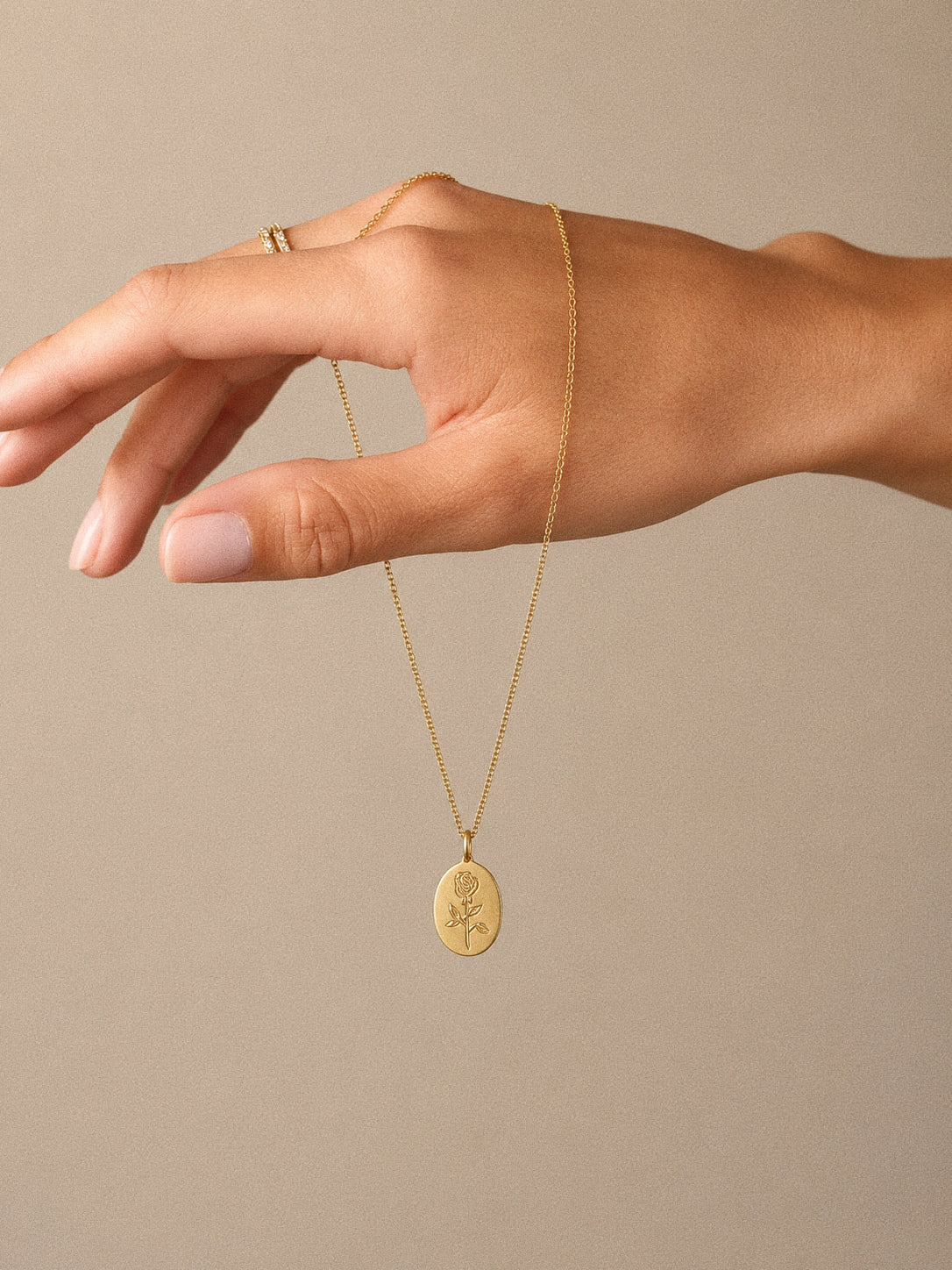 Gold rose pendant necklace draped over a hand to show the dainty oval medallion and chain