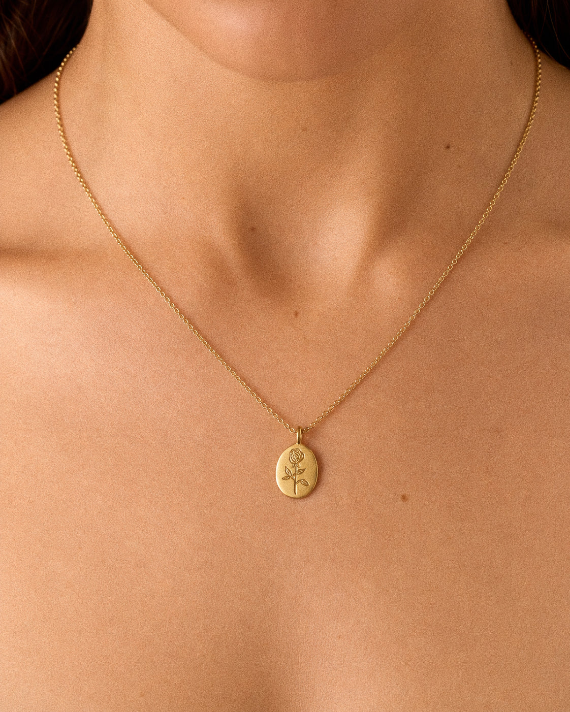 Woman wearing a dainty gold rose pendant necklace at the collarbone