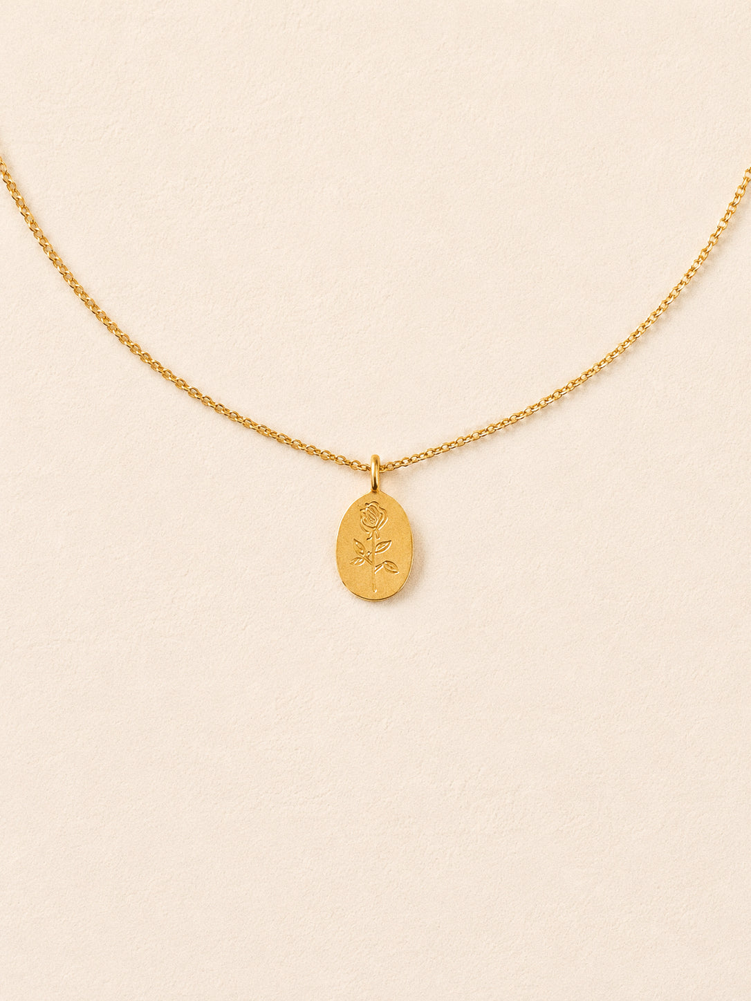 Gold oval rose pendant necklace on a fine cable chain against a cream background