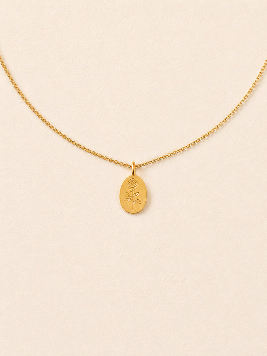 Gold oval rose pendant necklace on a fine cable chain against a cream background