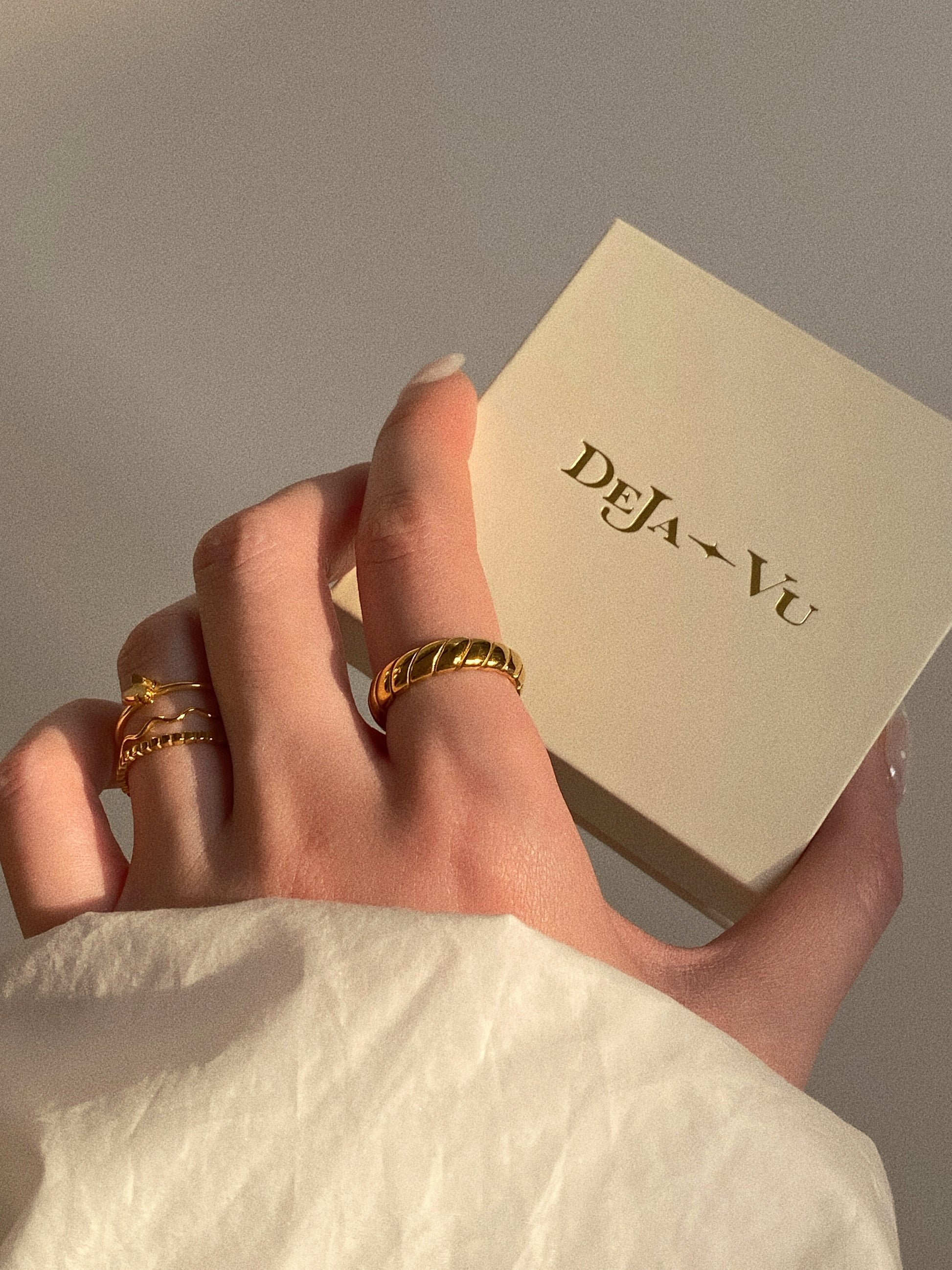 A woman showing her ring stack with the Deja vu gold croissant ring and a branded jewellery box.