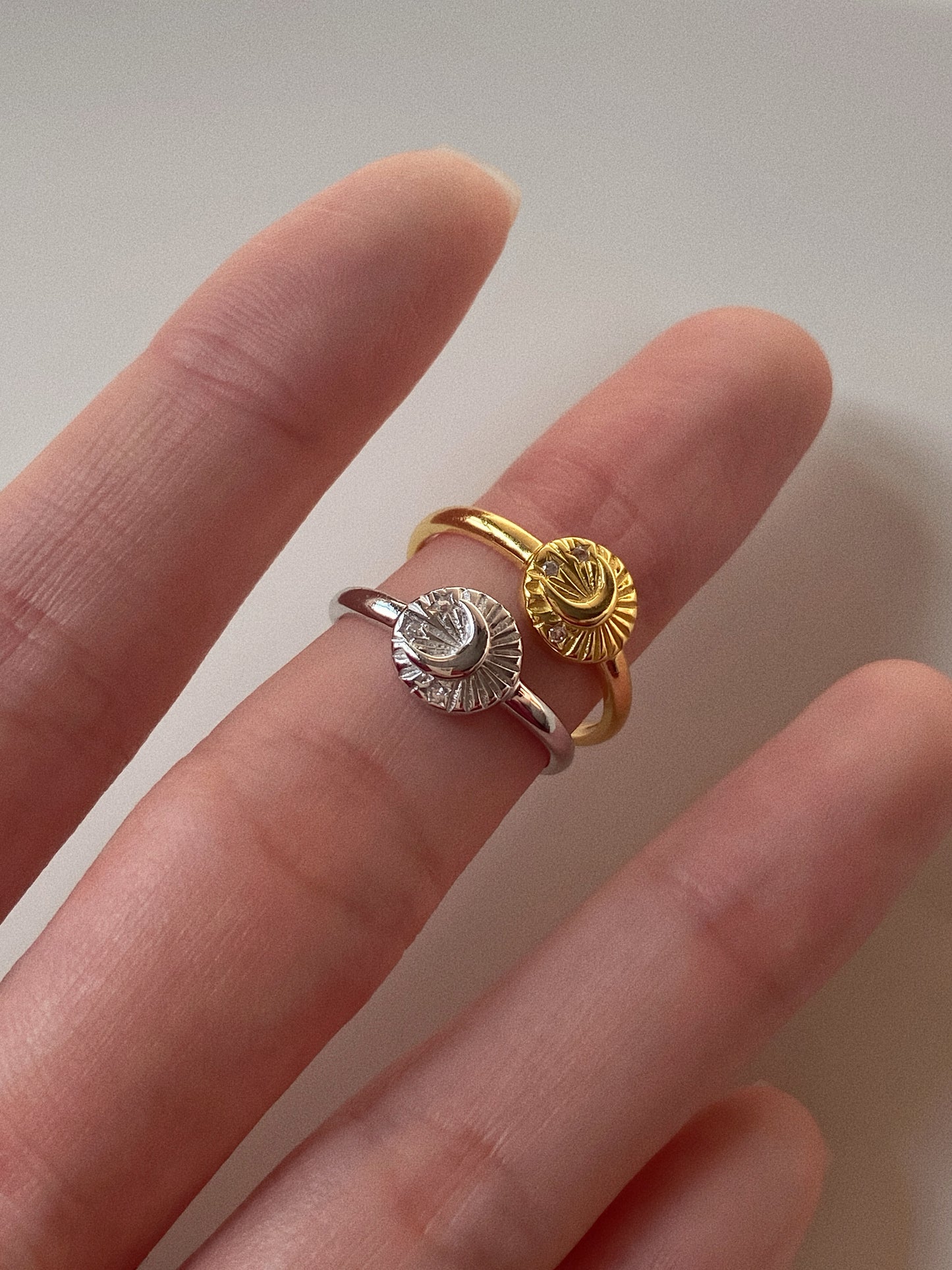 Close-up of both the gold and silver adjustable celestial rings held on fingers to show the high-shine finish.