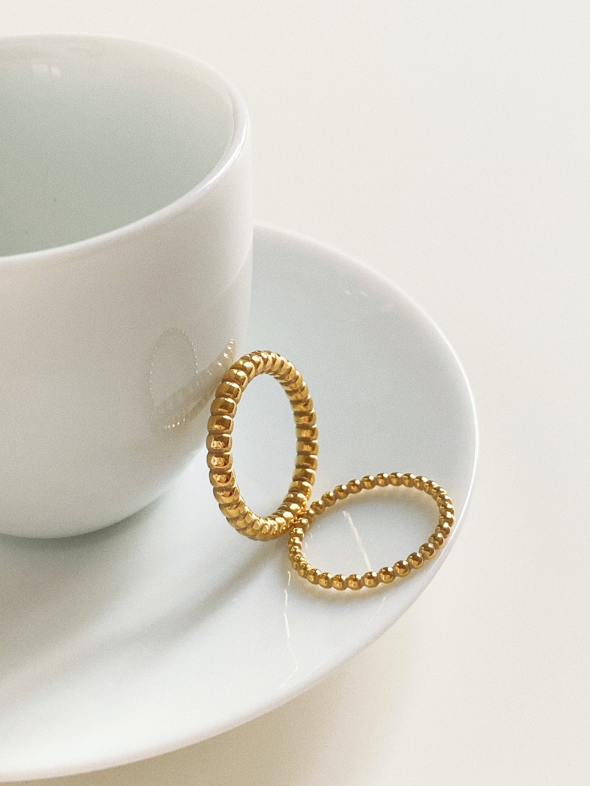 A collection of gold stacking rings including the beaded band in a white porcelain cup.