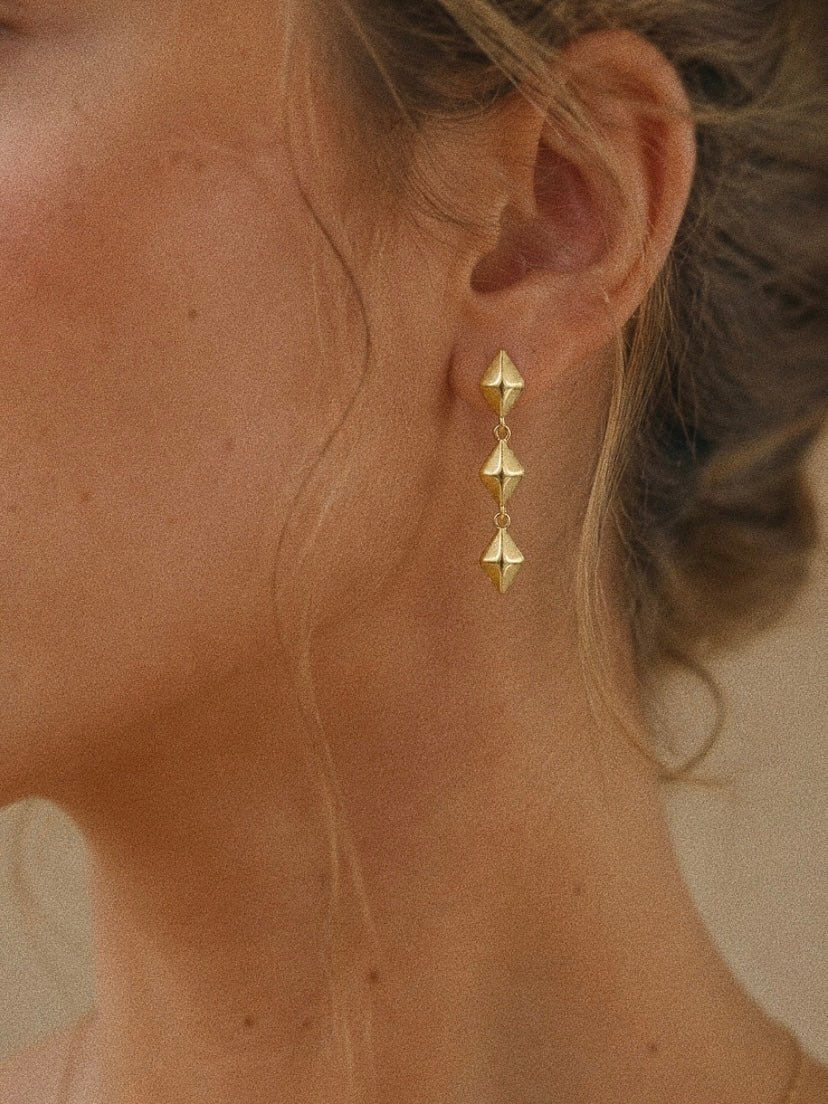 Vega gold star drop earring worn in the lobe, three faceted stars hanging in a straight 3 cm line.