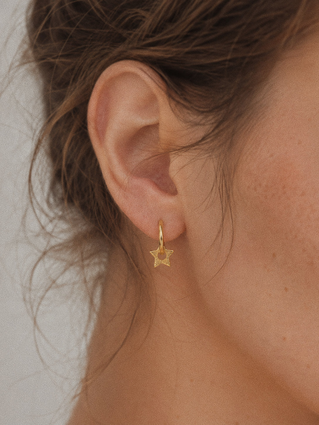 Nova gold star huggie hoop earring worn in the lobe, engraved star charm swinging just below the hoop.