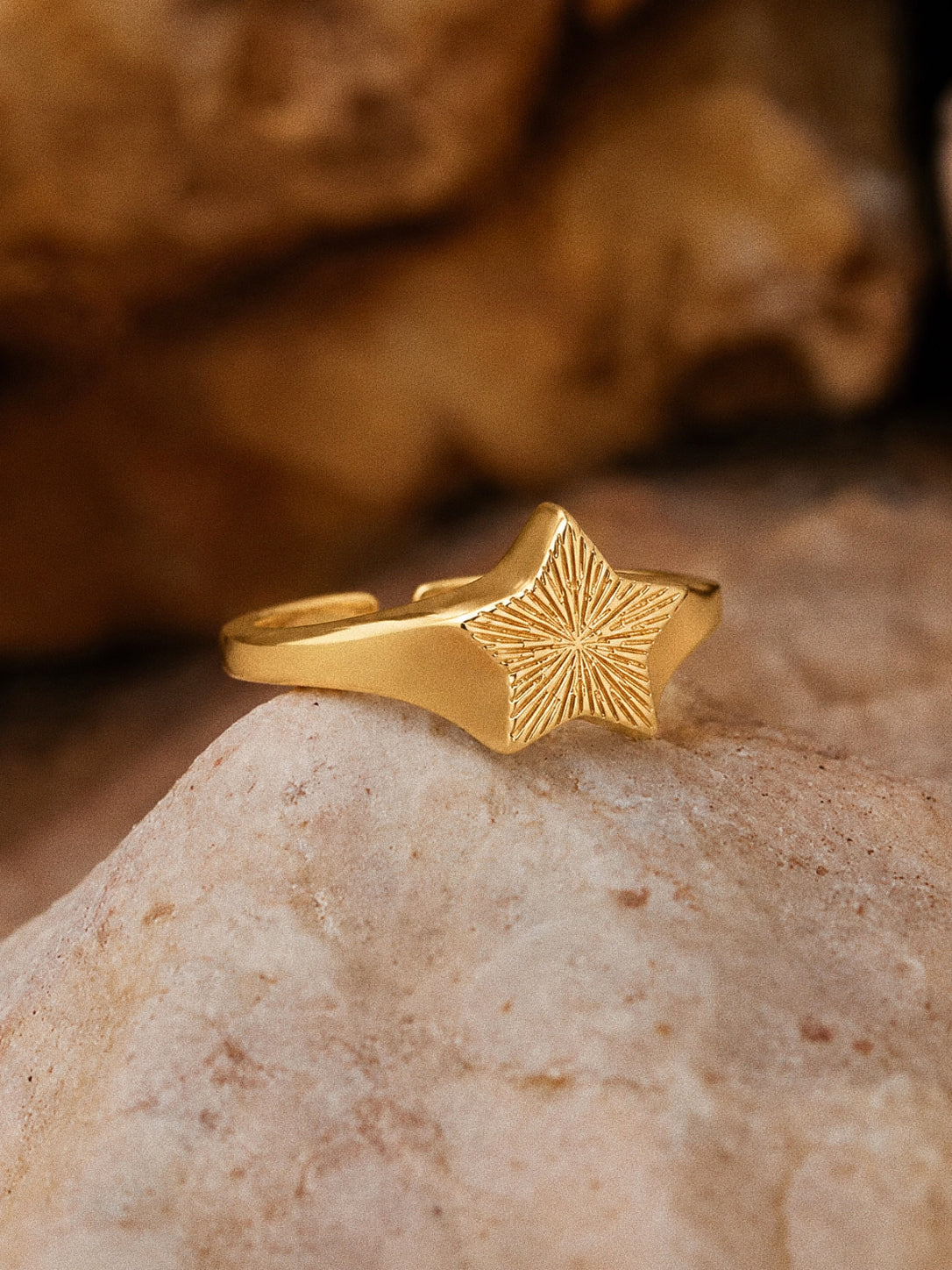 Gold star signet ring resting on pale stone in warm light, its engraved sunburst face turned to the sun.