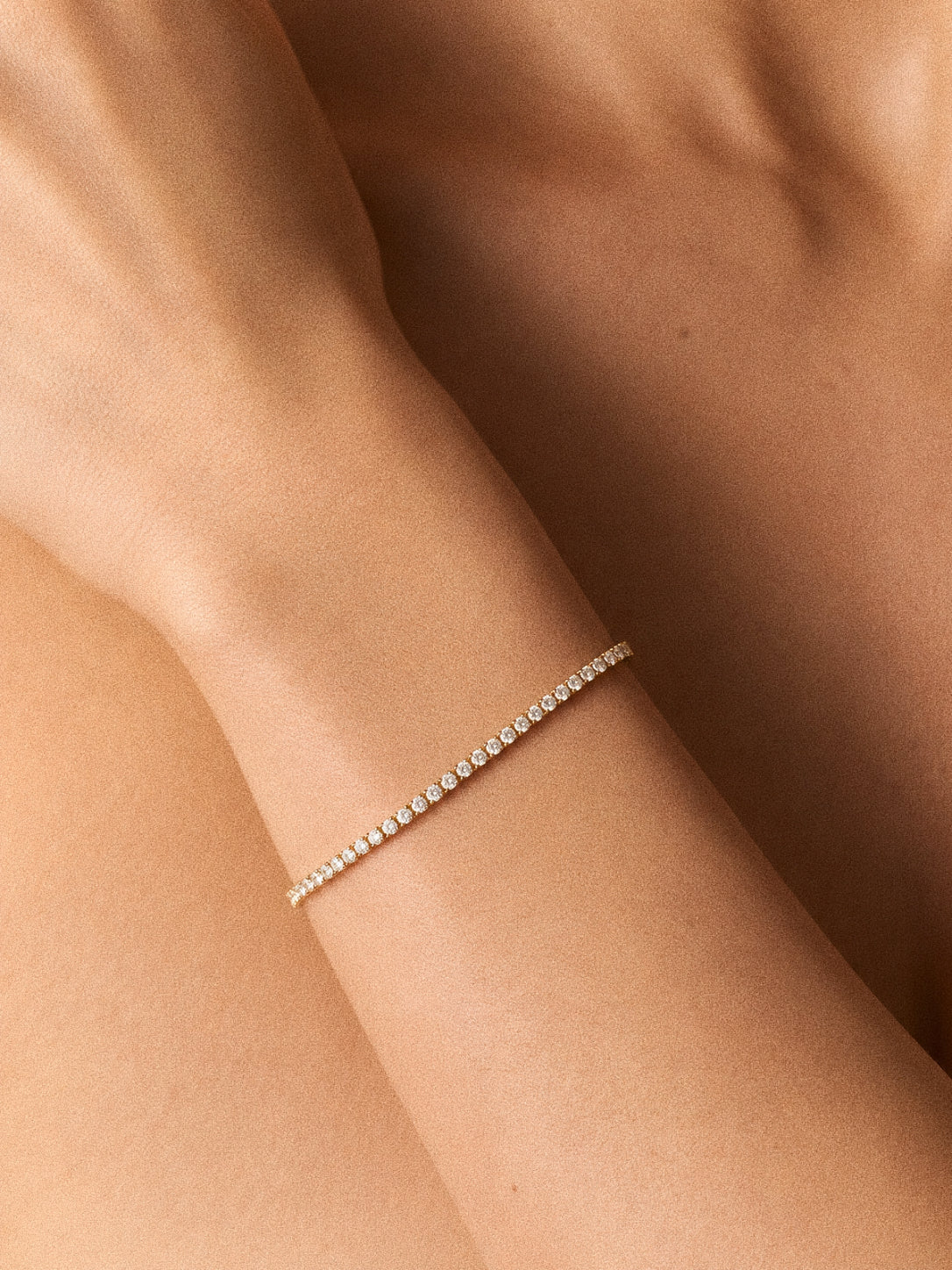 Model wearing a dainty gold cubic zirconia tennis bracelet on the wrist in warm natural light
