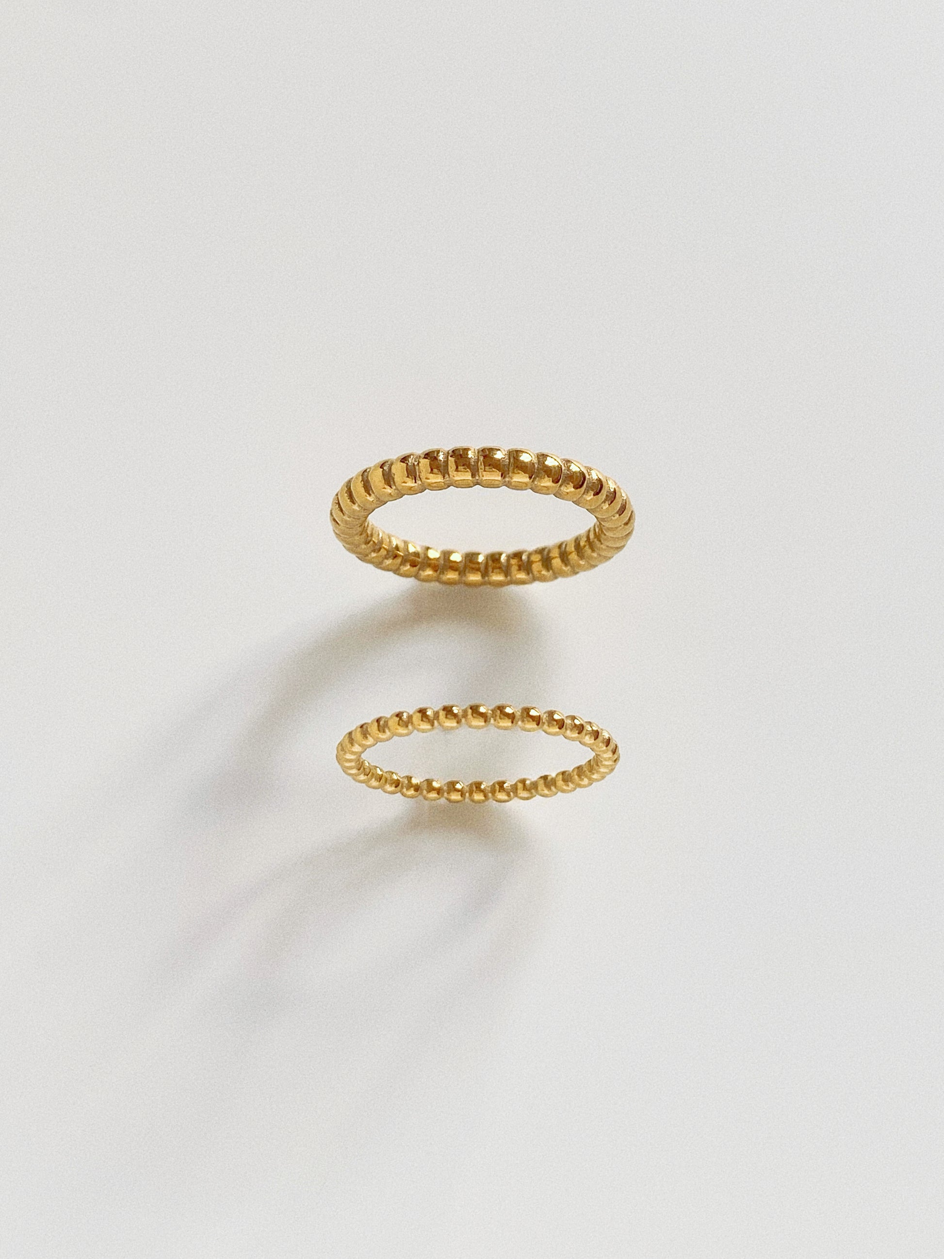 Comparison view of wide and narrow gold beaded rings in 18k gold plated titanium.