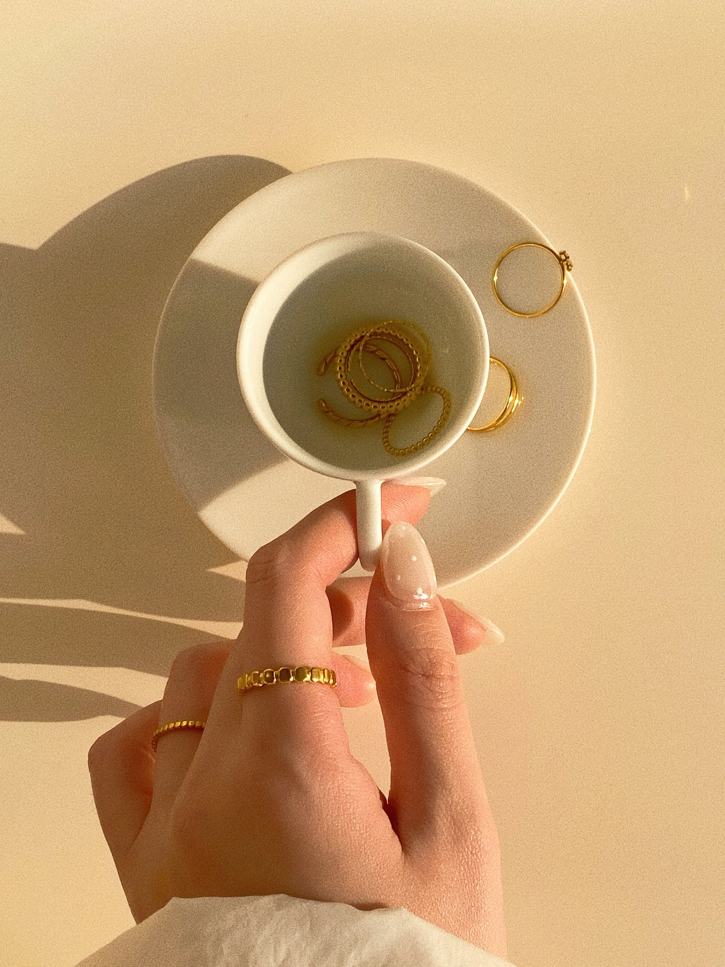 Top-down lifestyle view of a woman's hand wearing stacked gold rings including the beaded oval band.