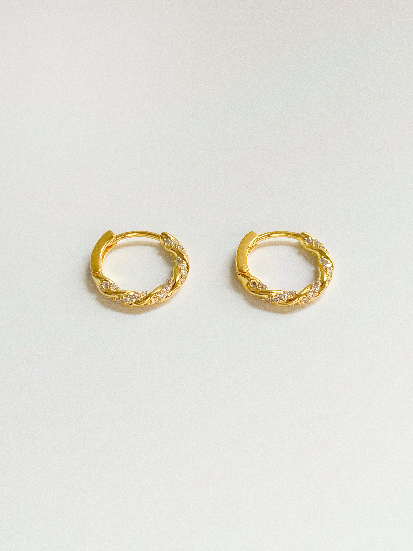 Small gold twisted hoop earrings with sparkling CZ stones, top angle view showing twist detail