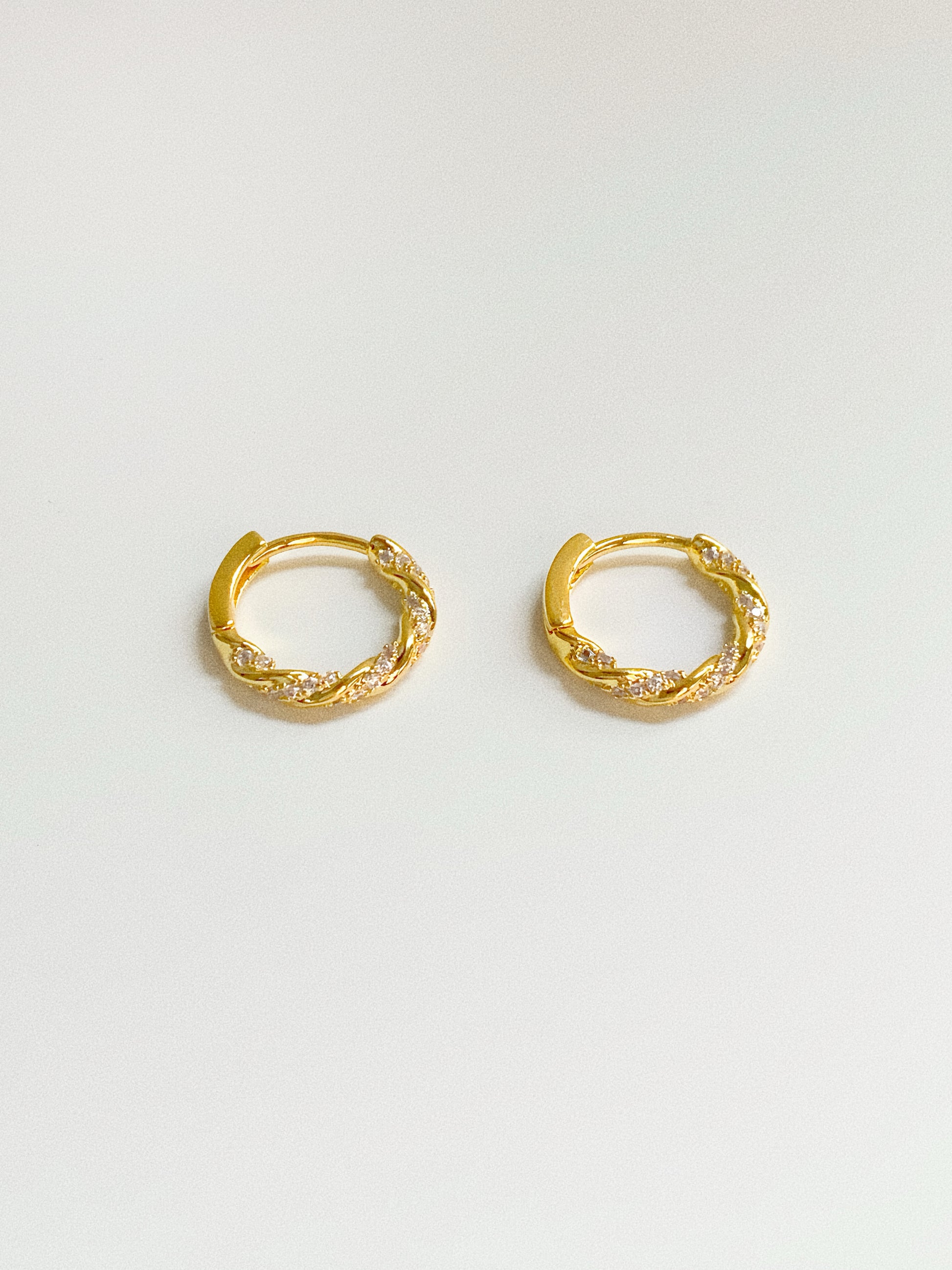 Small gold twisted hoop earrings with sparkling CZ stones, top angle view showing twist detail