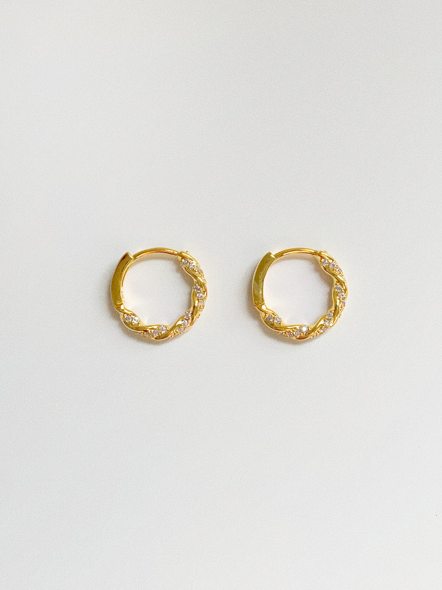 Gold twisted huggie hoop earrings with cubic zirconia pavé stones, front view on white background