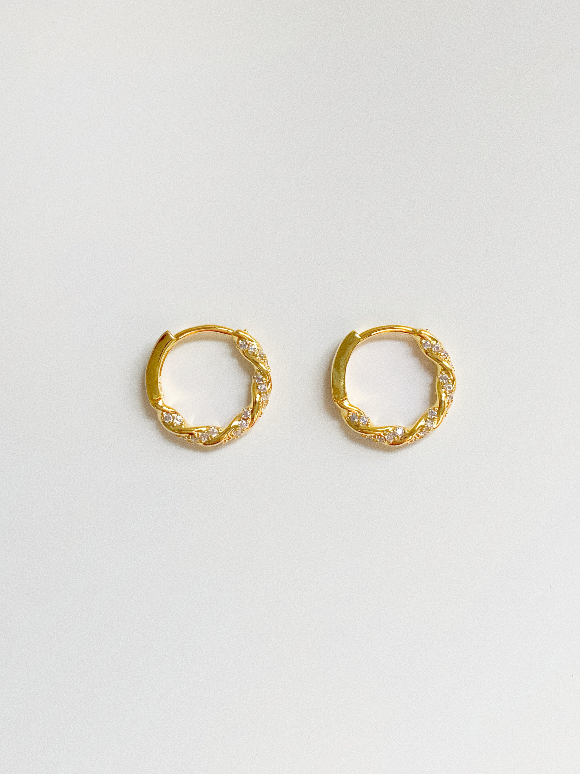 Gold twisted huggie hoop earrings with cubic zirconia pavé stones, front view on white background