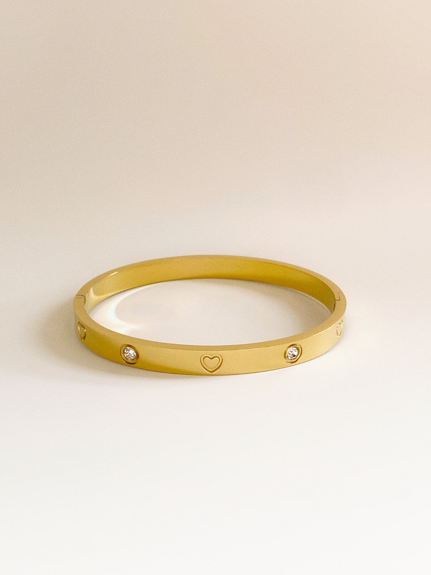 Isolated view of gold oval hinge bangle showing the 0.6cm width and crystal heart details.
