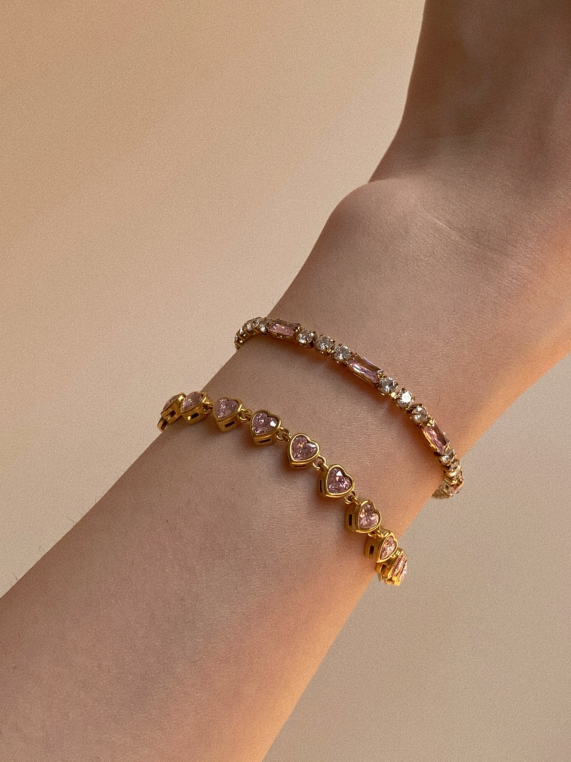 Close up of waterproof gold tennis bracelet featuring pink heart-shaped cubic zirconia stones.