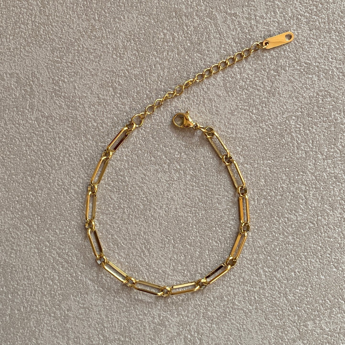 Flat-lay of adjustable gold paperclip bracelet with extender chain and clasp, tarnish-resistant stainless steel