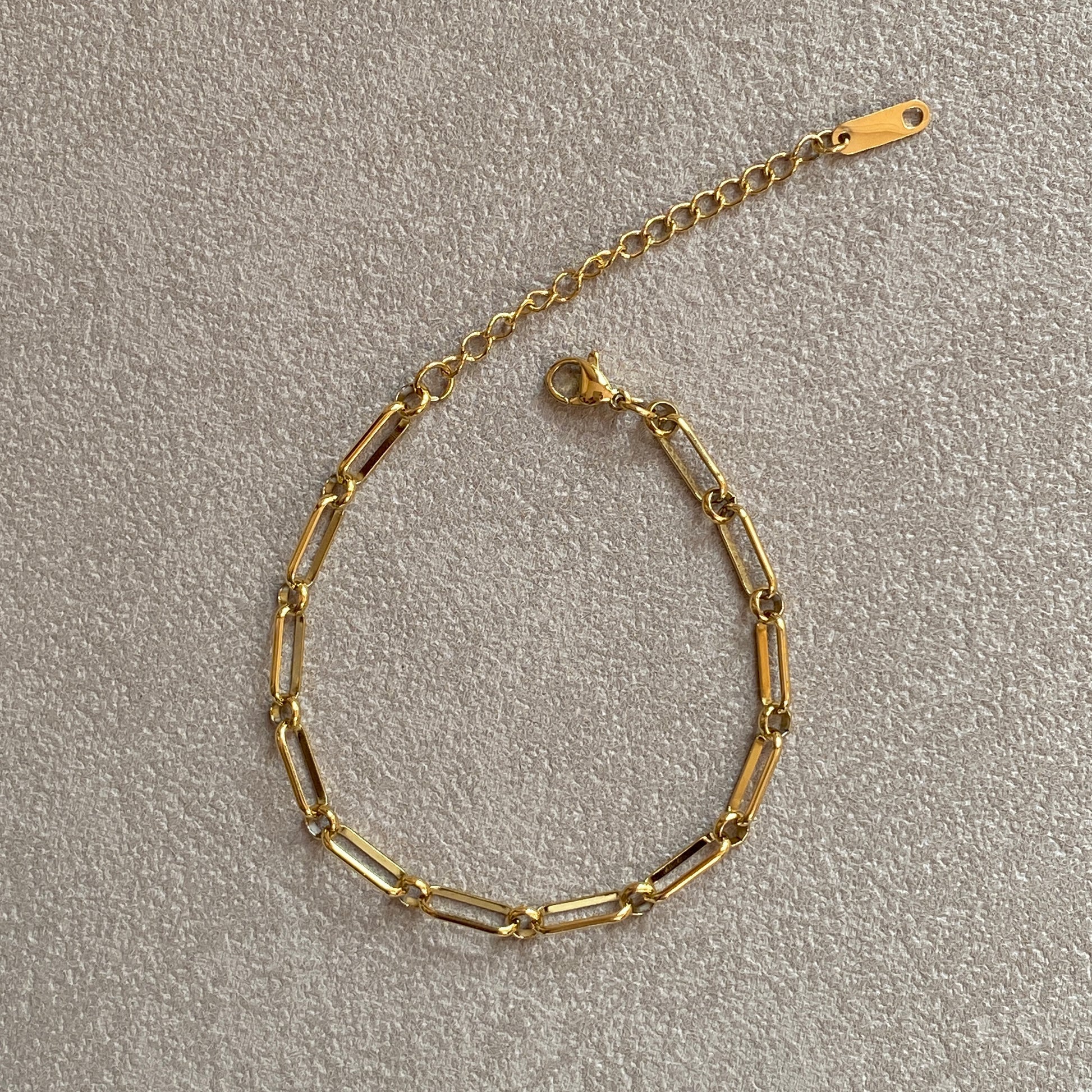 Flat-lay of adjustable gold paperclip bracelet with extender chain and clasp, tarnish-resistant stainless steel