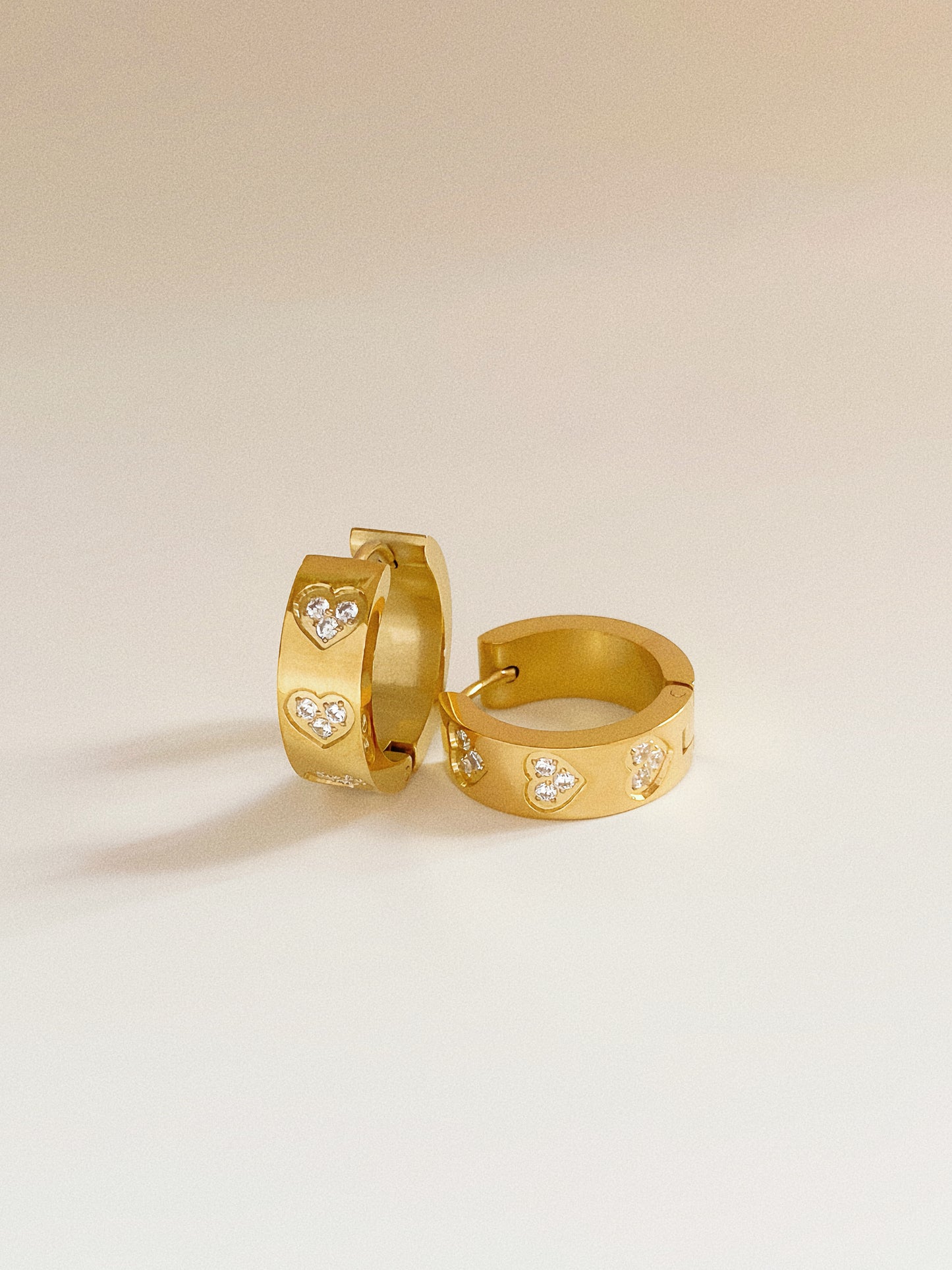 Isolated pair of wide gold hoop earrings, 1.7cm height, featuring three cubic zirconia hearts.