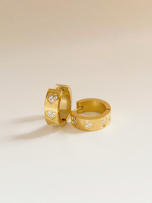 Isolated pair of wide gold hoop earrings, 1.7cm height, featuring three cubic zirconia hearts.