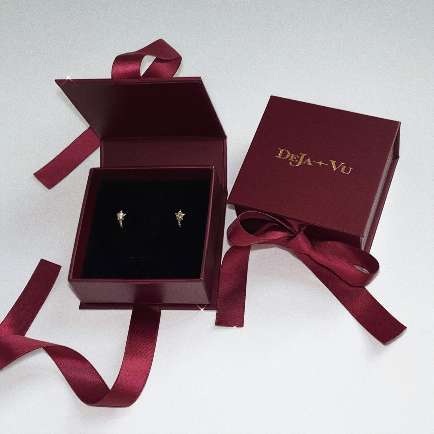 Deja vu Jewellery burgundy gift box containing a pair of gold star huggie earrings, perfect for gifting.