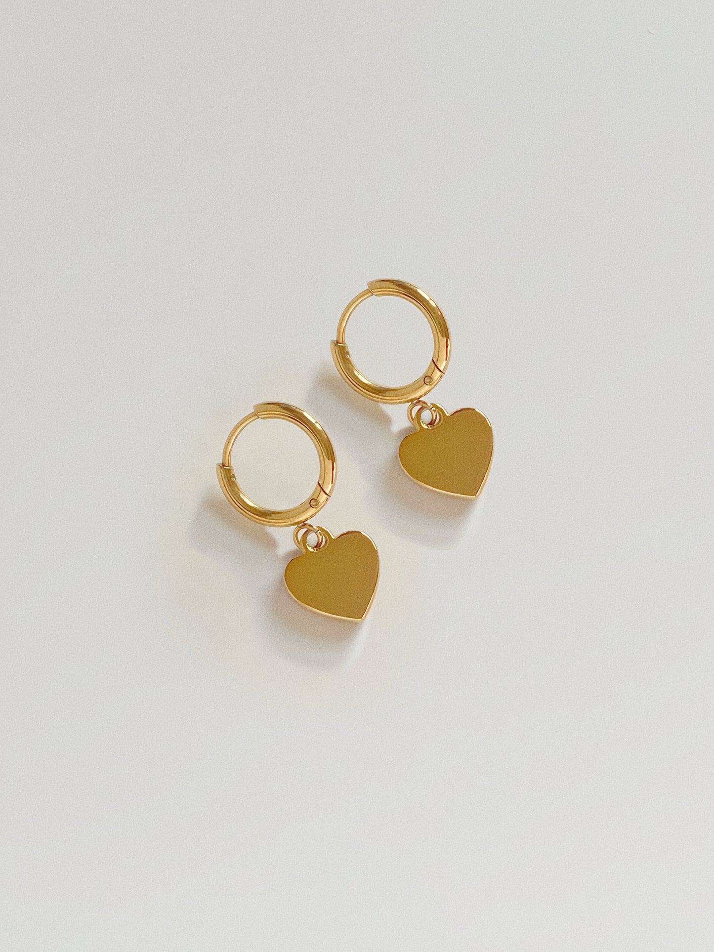 Back view of the heart charm earrings showing the polished 18k gold plated surface, offering a reversible look.