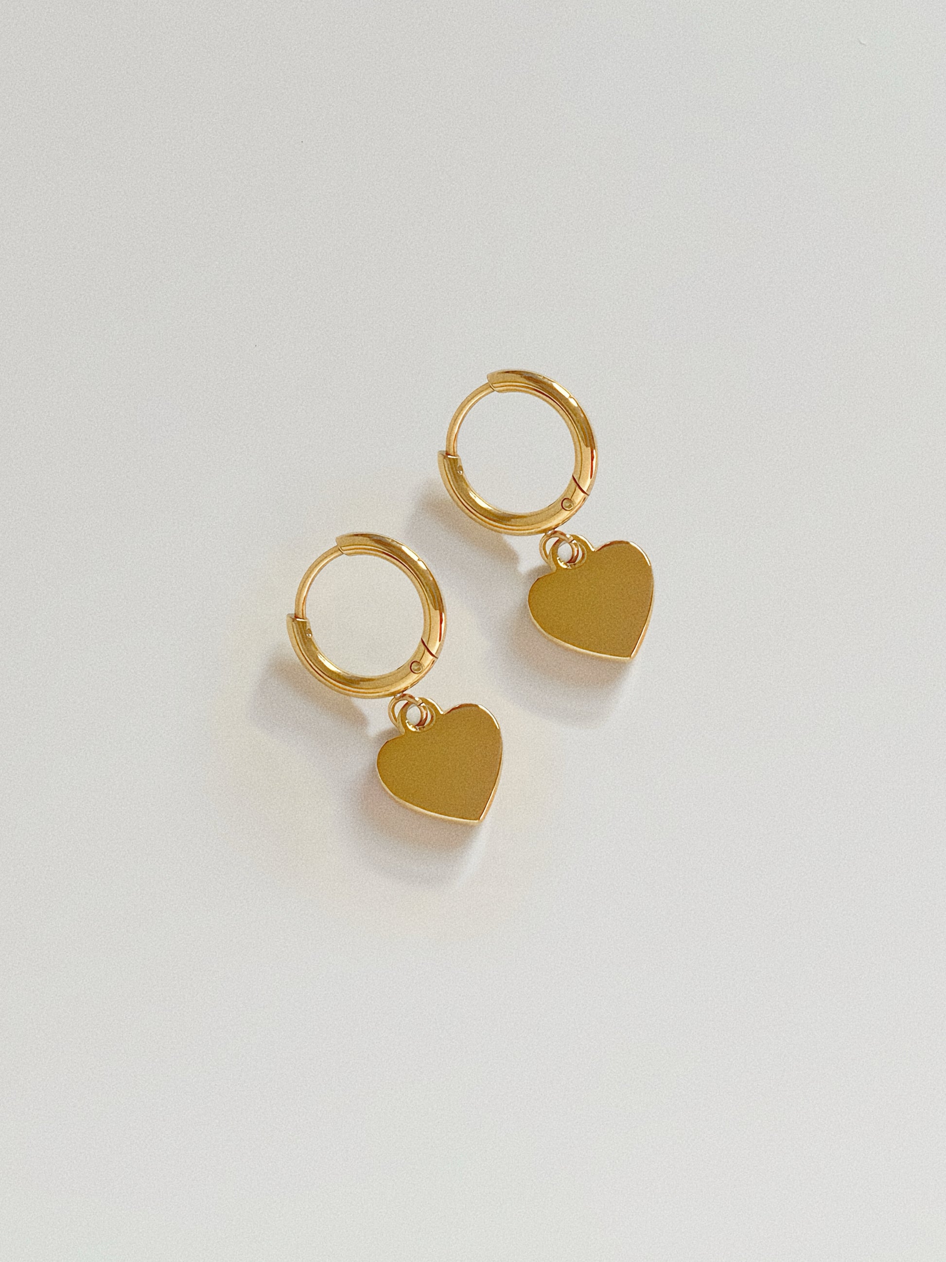 Back view of the heart charm earrings showing the polished 18k gold plated surface, offering a reversible look.