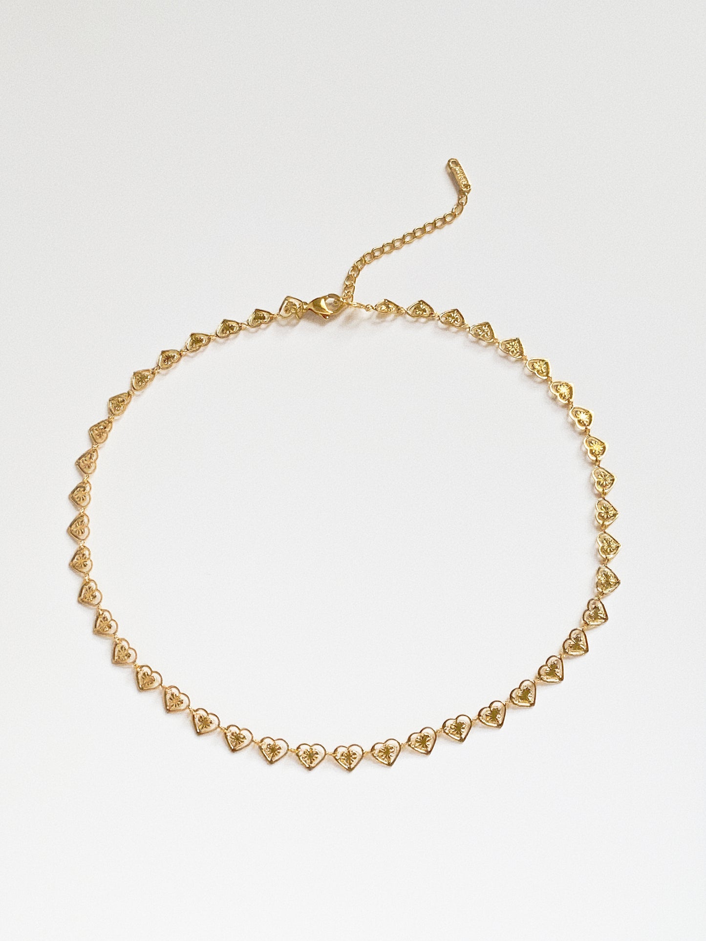 Flat lay view of the gold heart link choker arranged in a circle, showing the continuous reflective diamond-cut texture.
